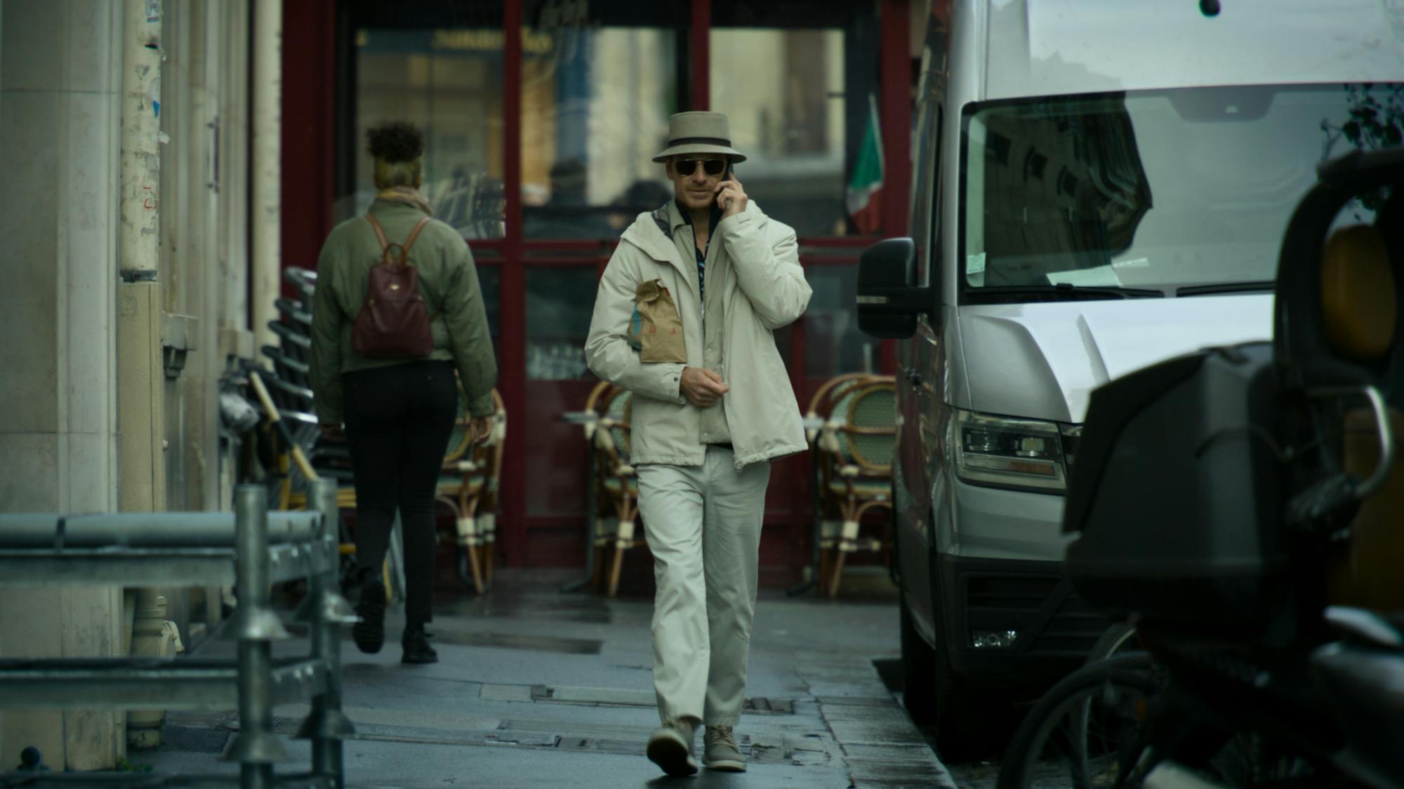 The Killer (Michael Fassbender) in The Killer walks through a street wearing a beige outfit.