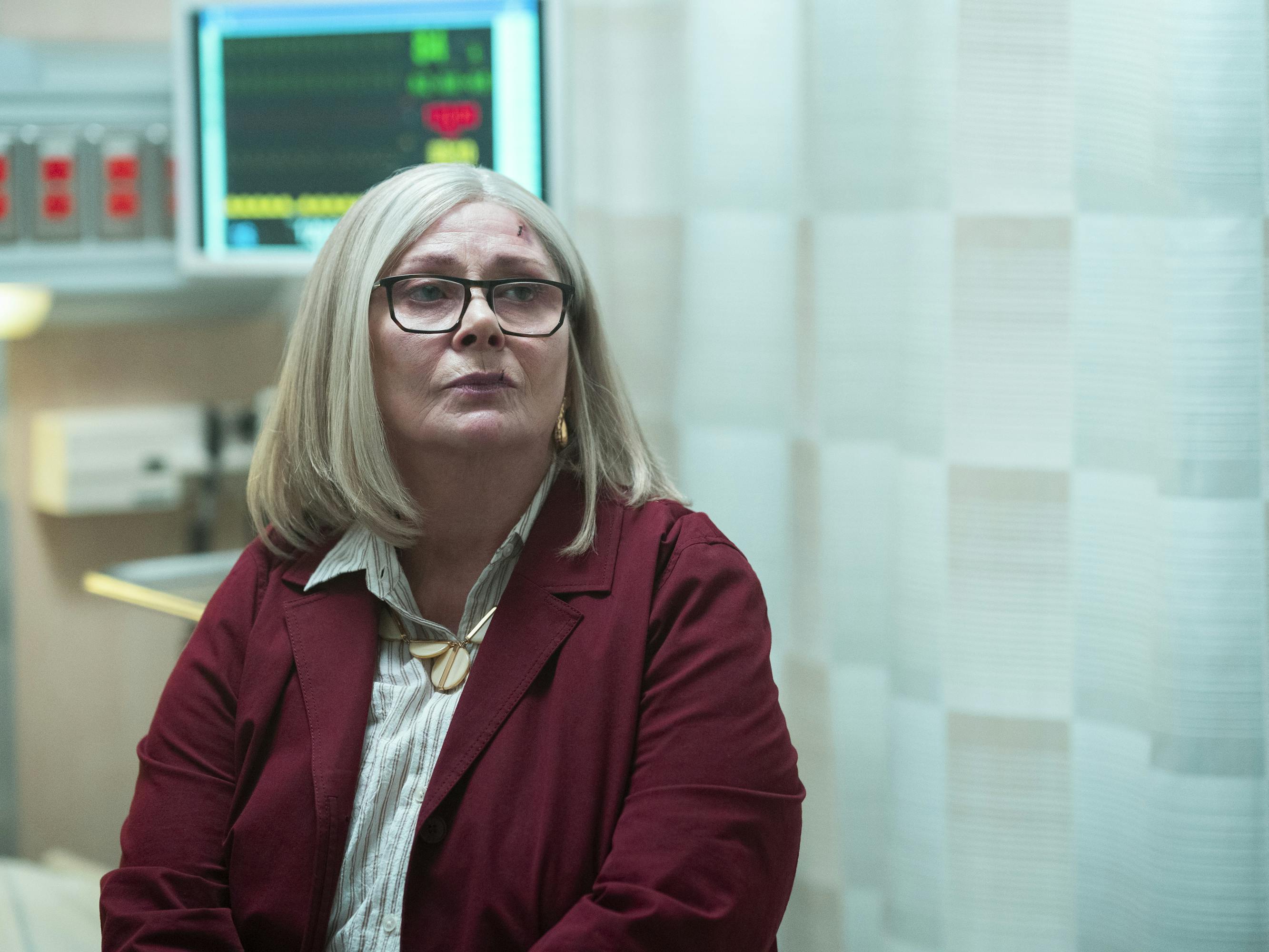 Ruth Brenner (Elizabeth Ashley) sits in a hospital room wearing a maroon coat.