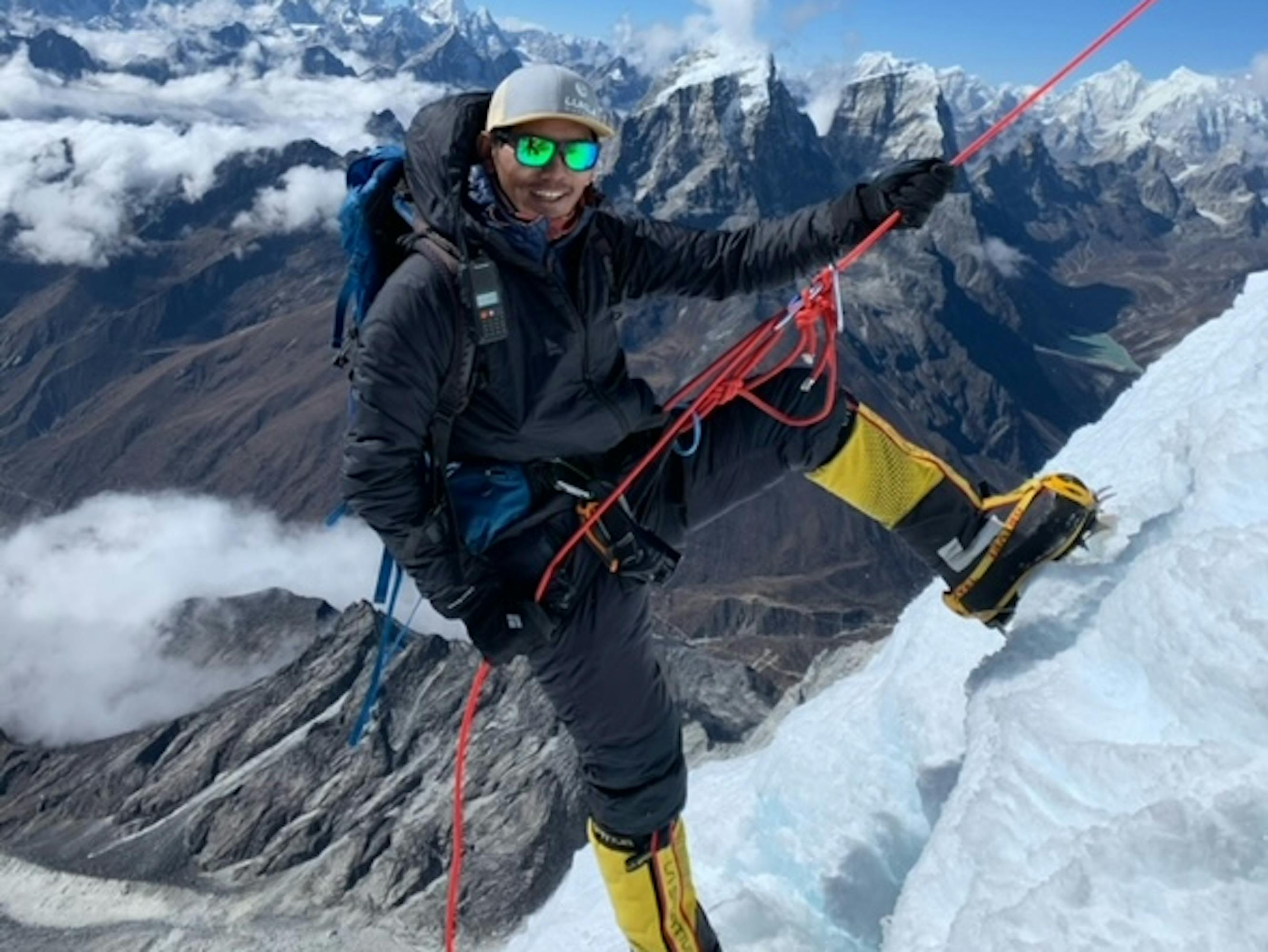 Gesman Tamang holds a red rope and smiles from a cliffside.