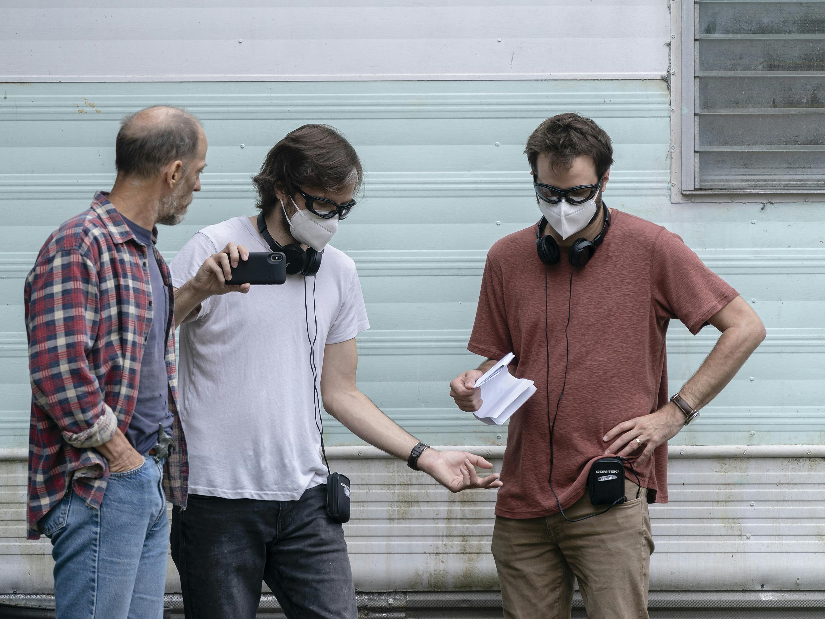 Matt and Ross Duffer work behind the scenes with a man in a flannel and jeans. The two directors wear PPE and tshirts.