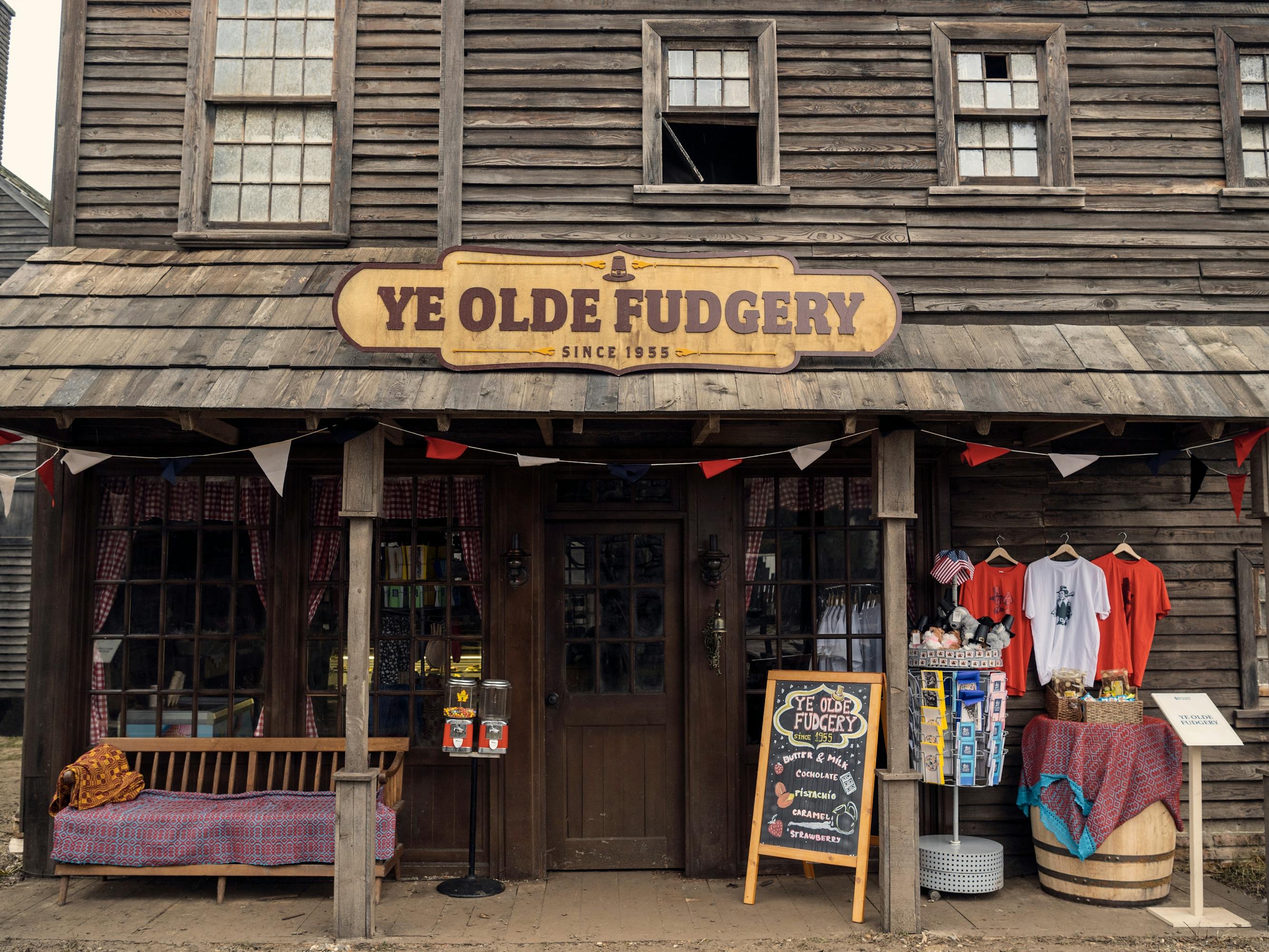 Jericho's Ye Olde Fudgery. There is a yellow sign with brown font and merch on a rack outside.