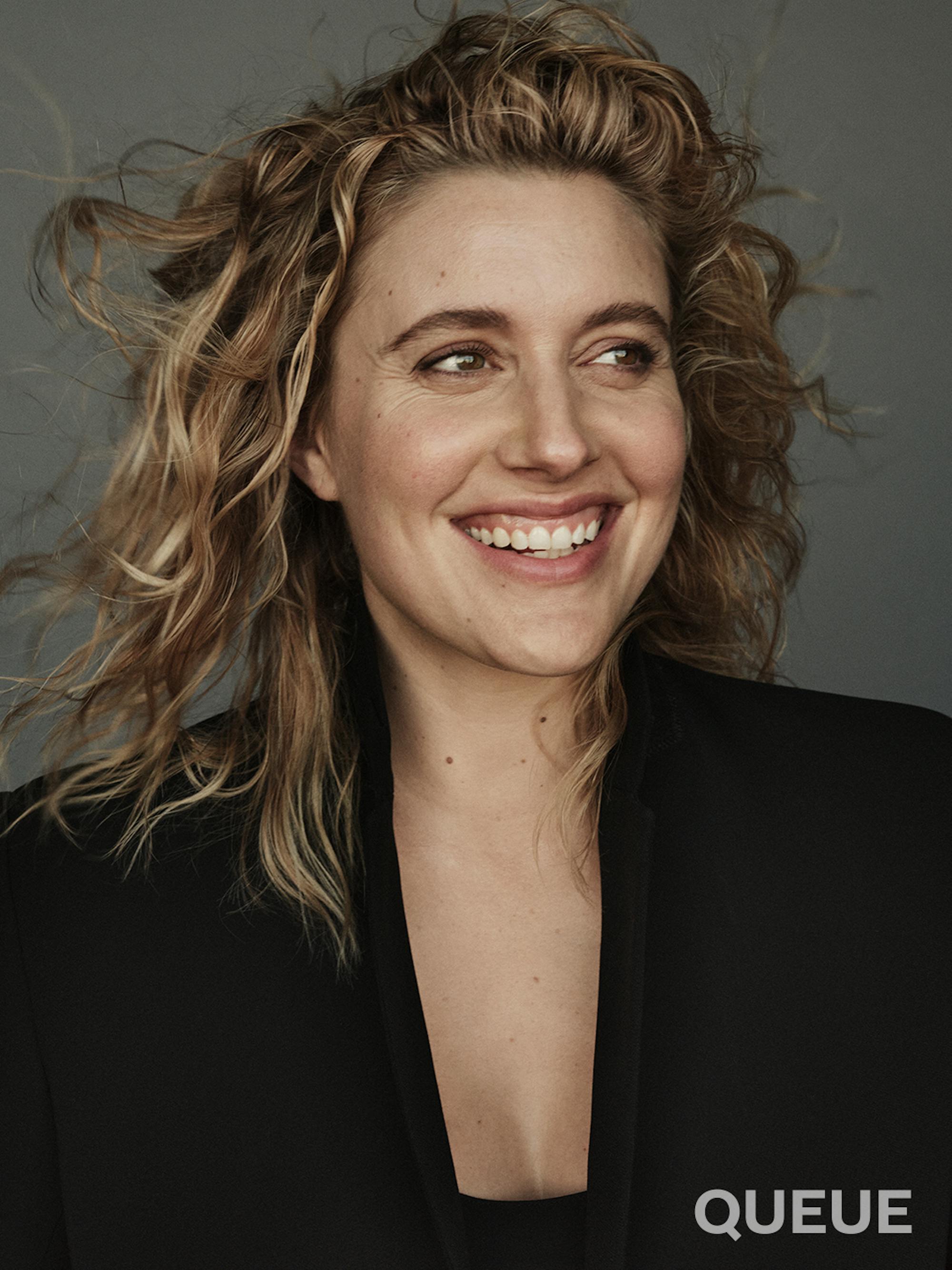 Greta Gerwig wears a black blazer and smiles at something off-camera on Queue's Issue 11 cover.