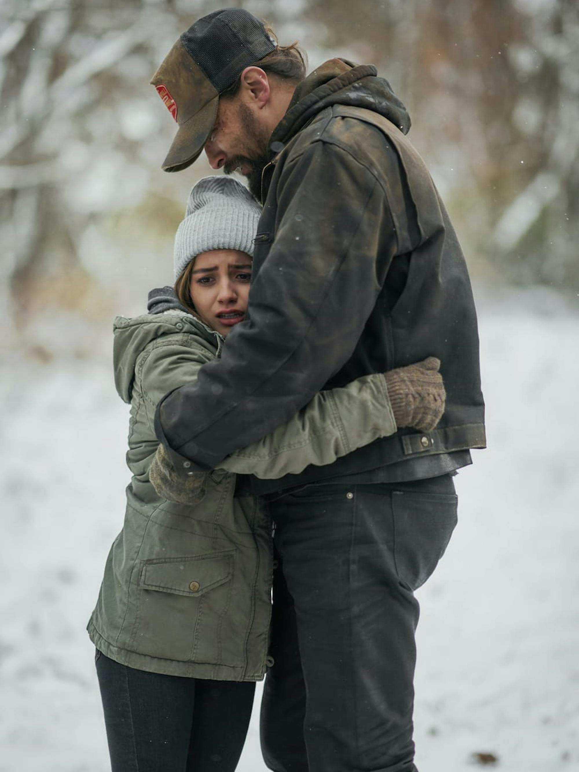 Rachel Cooper (Isabela Merced) and Ray Cooper (Jason Momoa) in Sweet Girl stand in a snowy field, bundled in dark coats and look afraid.