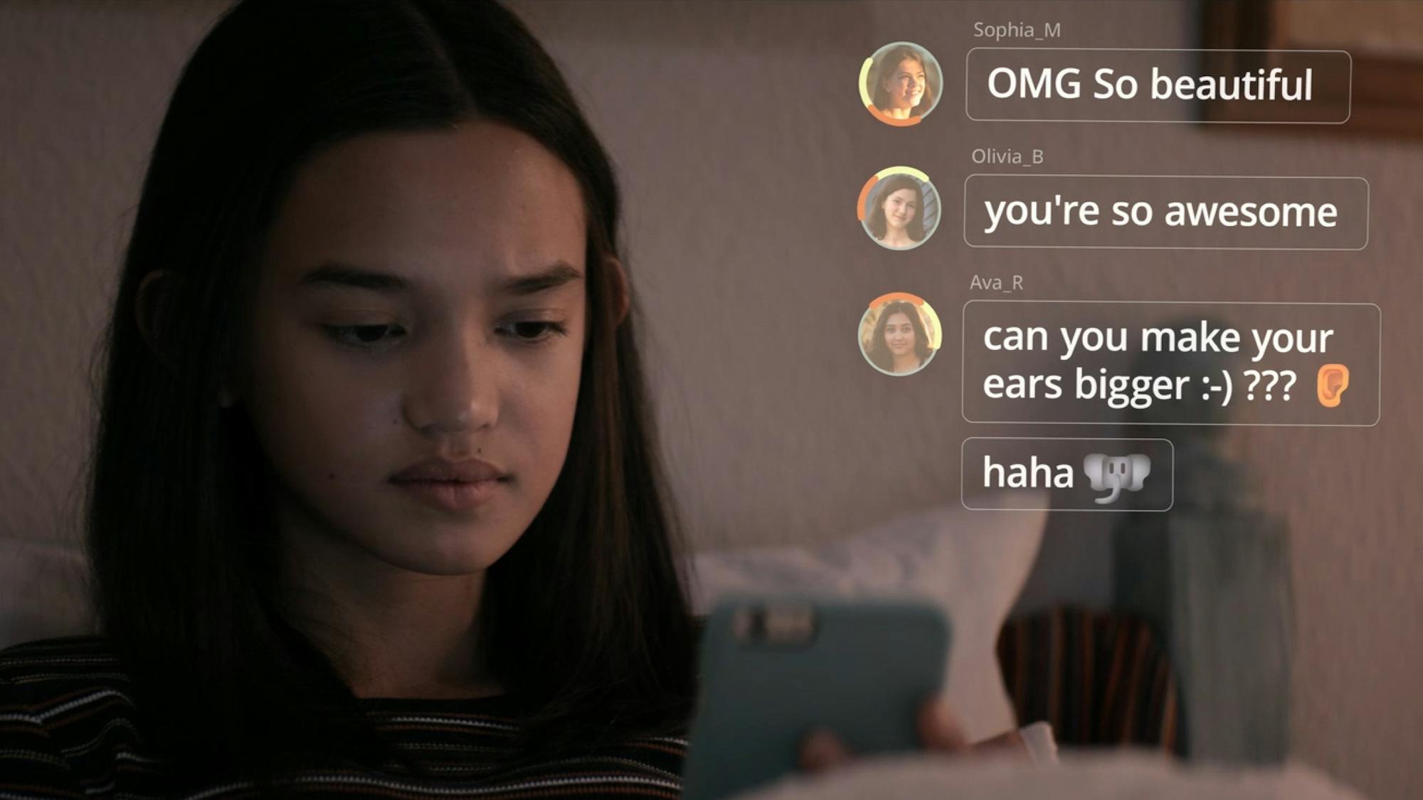 A young girl is pictured in her room, looking at her phone. Social media comments are superimposed on the frame, reading “OMG So beautiful”; “you’re so awesome”; and “Can you make your ears bigger?”