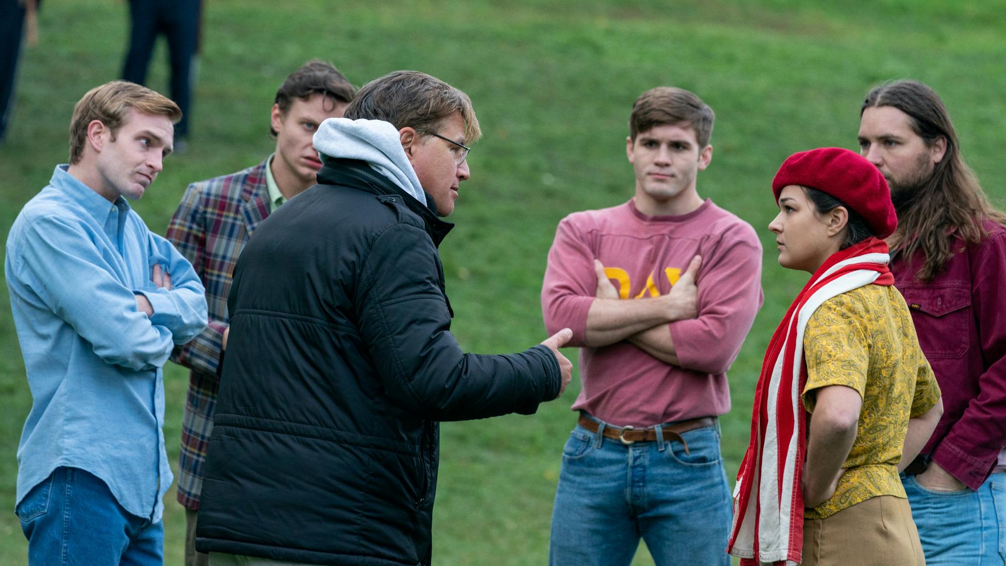 Extras circle around Aaron Sorkin as he prepares them for a protest scene in The Trial of the Chicago 7.