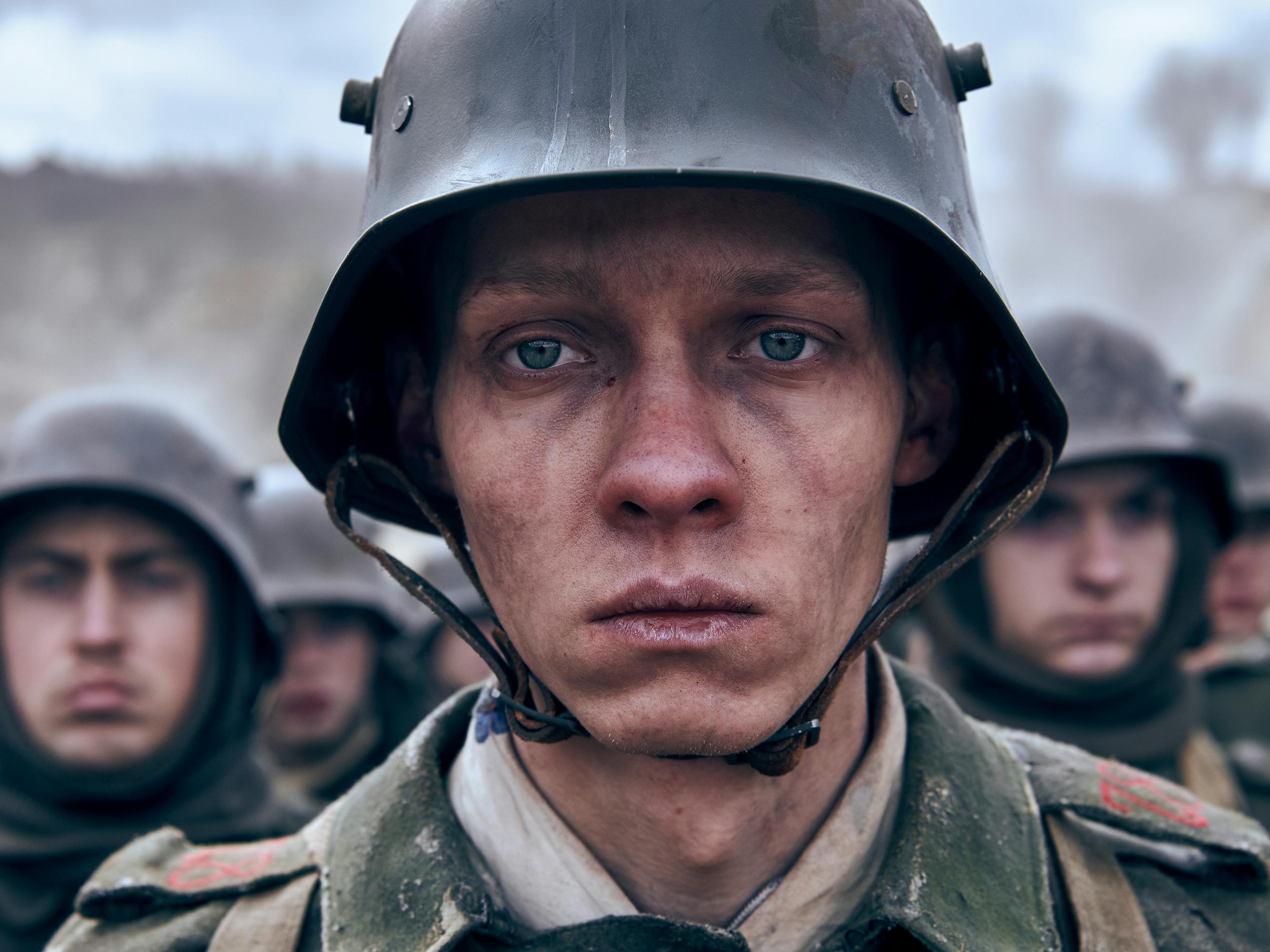 Paul Bäumer (Felix Kammerer) looks dejected, cold, and tired as he stands in a crowd of other uniform-wearing soldiers. 