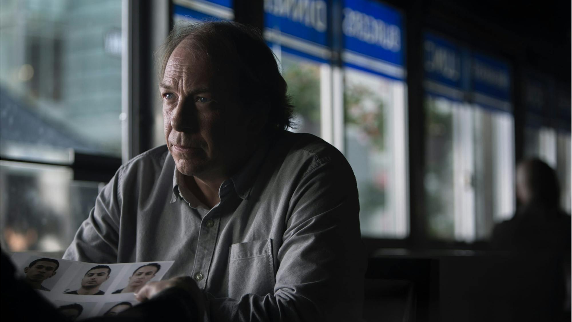 Bill Camp’s character, Dennis Box, in The Night Of, sits across from someone who holds a sheet with images of men, presumably suspects. Camp looks very serious, and wears a buttoned down shirt