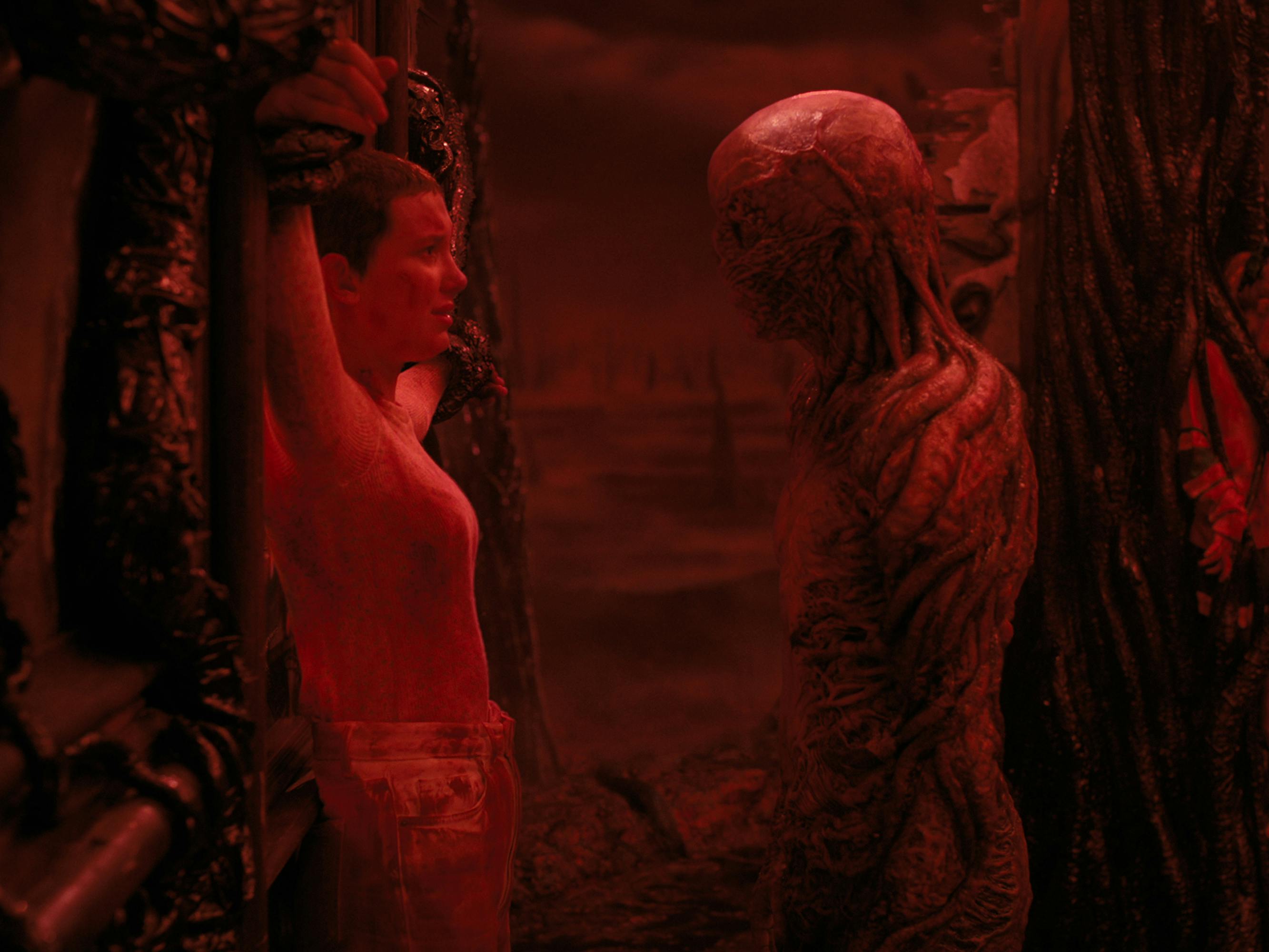 Eleven (Millie Bobby Brown) faces off with Vecna (Jamie Campbell Bower) in a red-lit scene. 