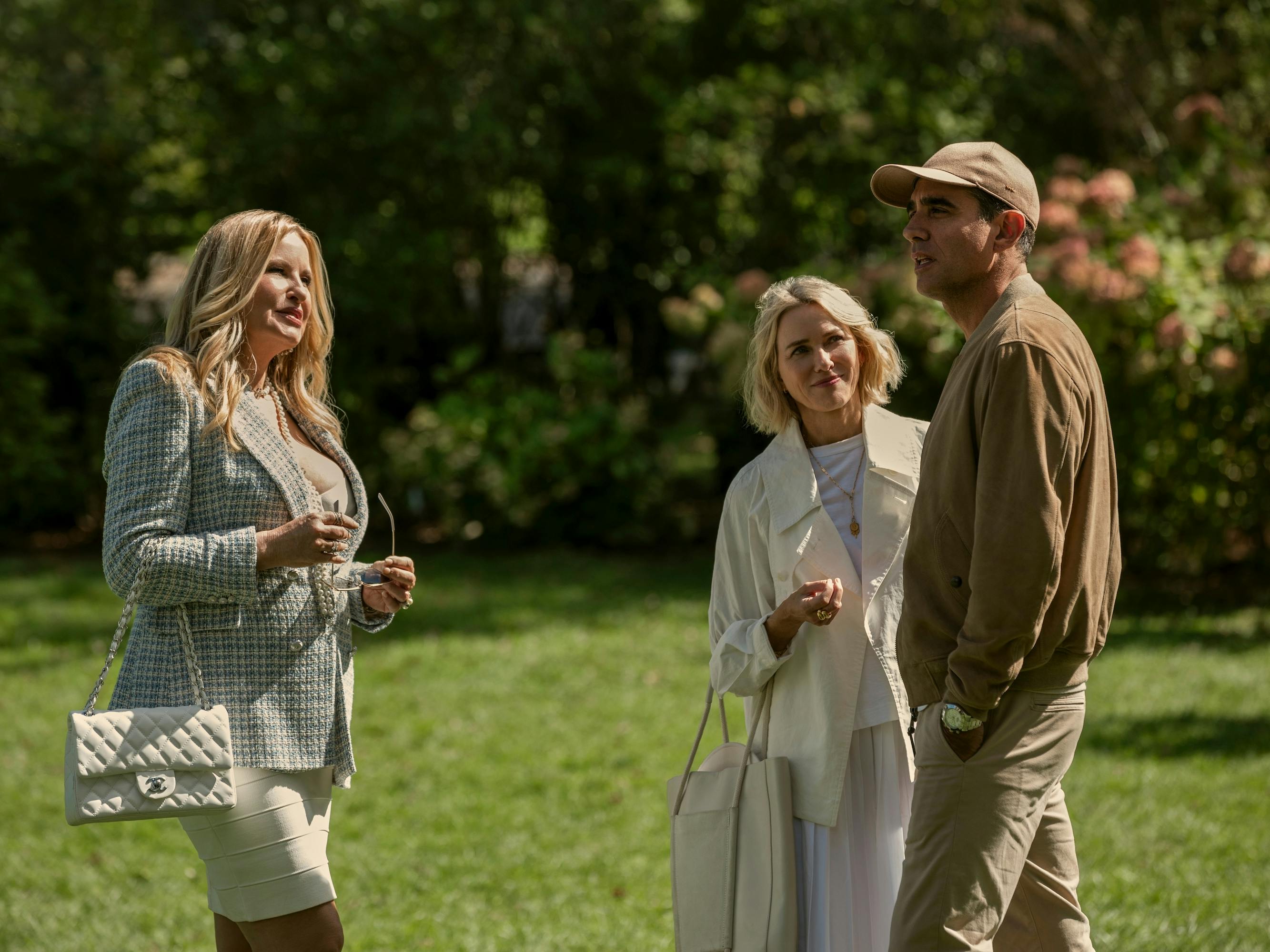 Karen Calhoun (Jennifer Coolidge), Nora Brannock (Naomi Watts), and Dean Brannock (Bobby Cannavale) stand in a bright green lawn.