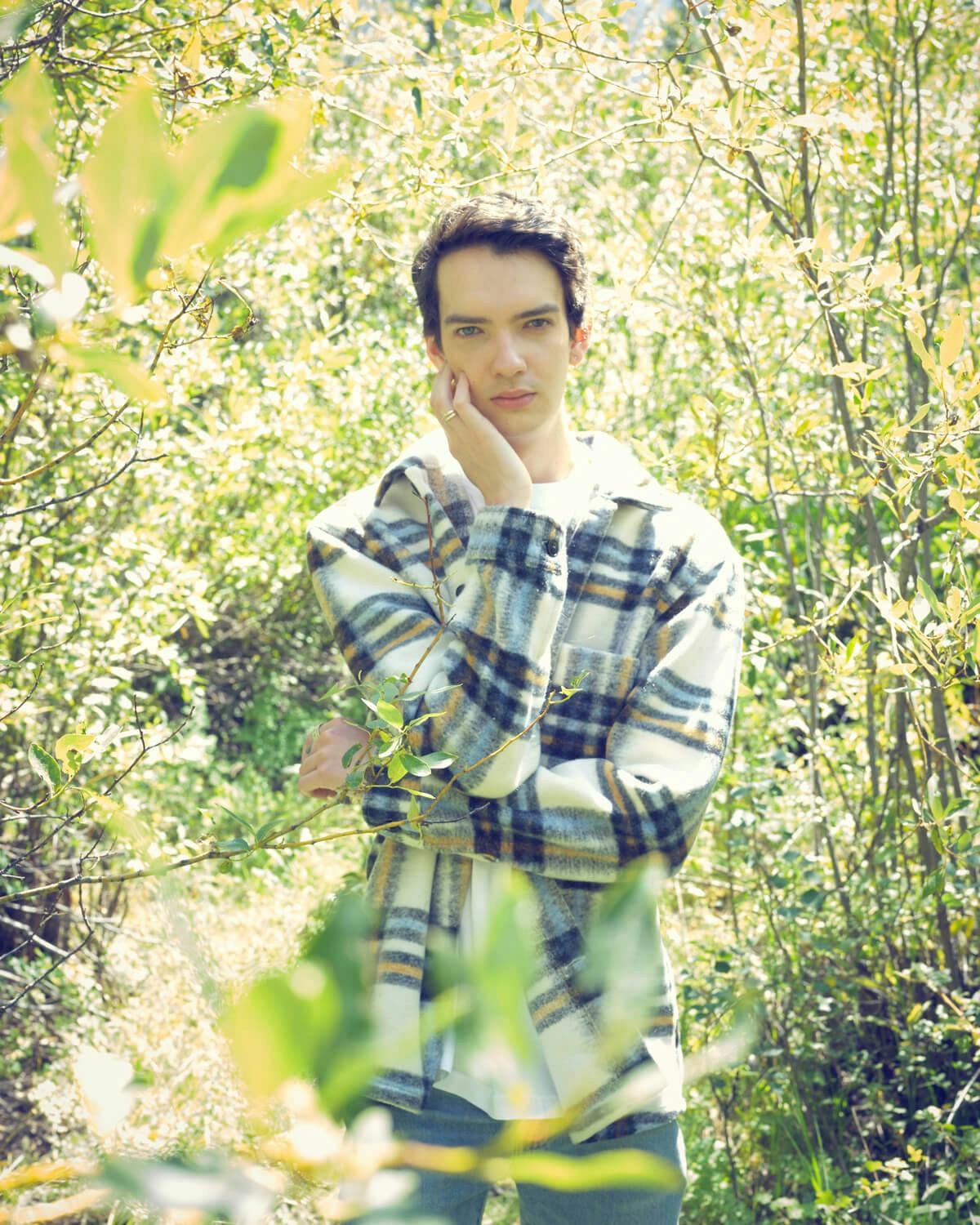 Kodi Smit-McPhee in a double-breasted blazer, blouse, jeans and boots in the woods of the Colorado mountains at the Telluride Film Festival, 2021.