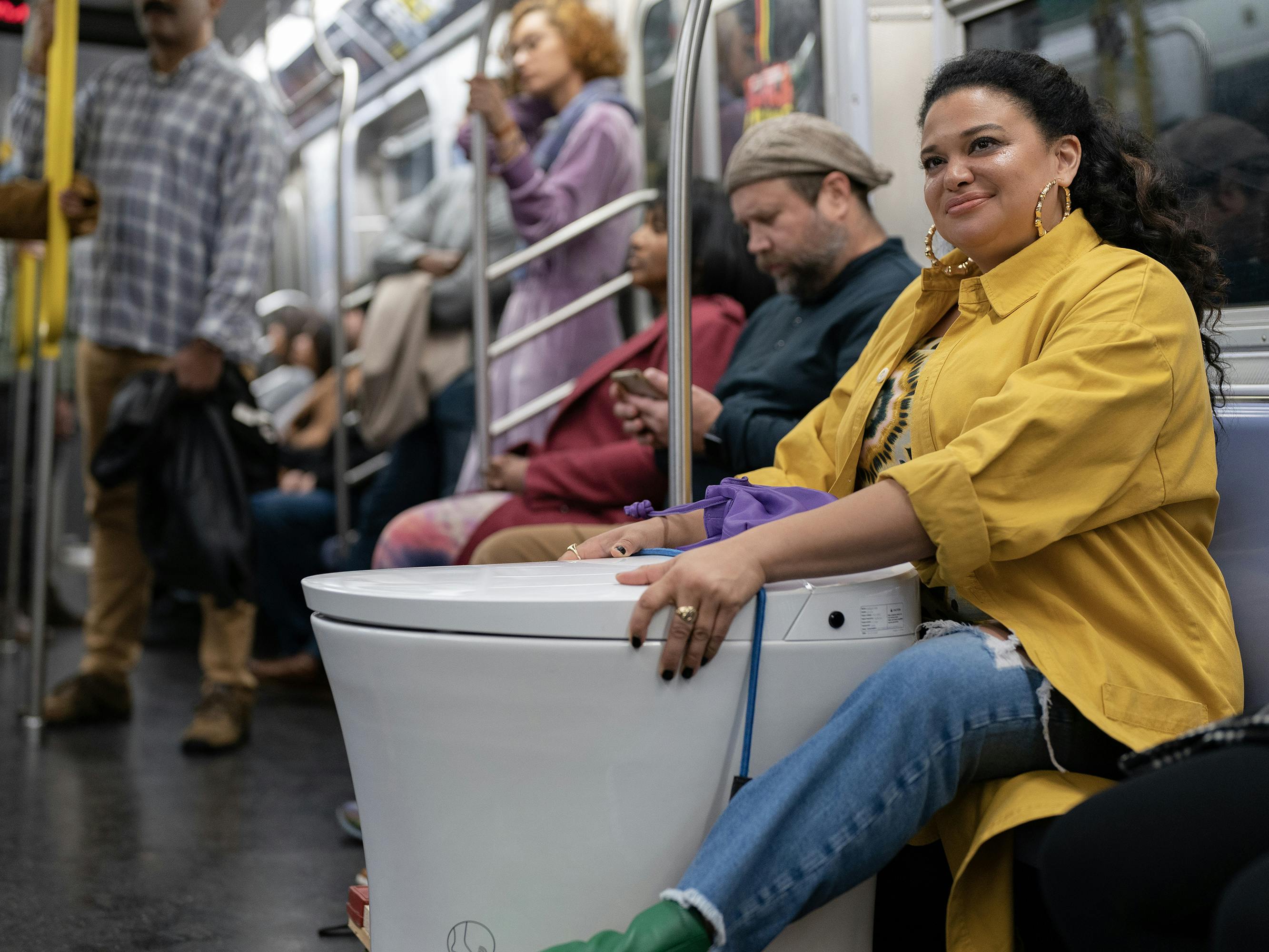 Mavis (Michelle Buteau) in Survival of the Thickest wears jeans, a yellow raincoat, and green shoes on the subway, straddling a toilet. 