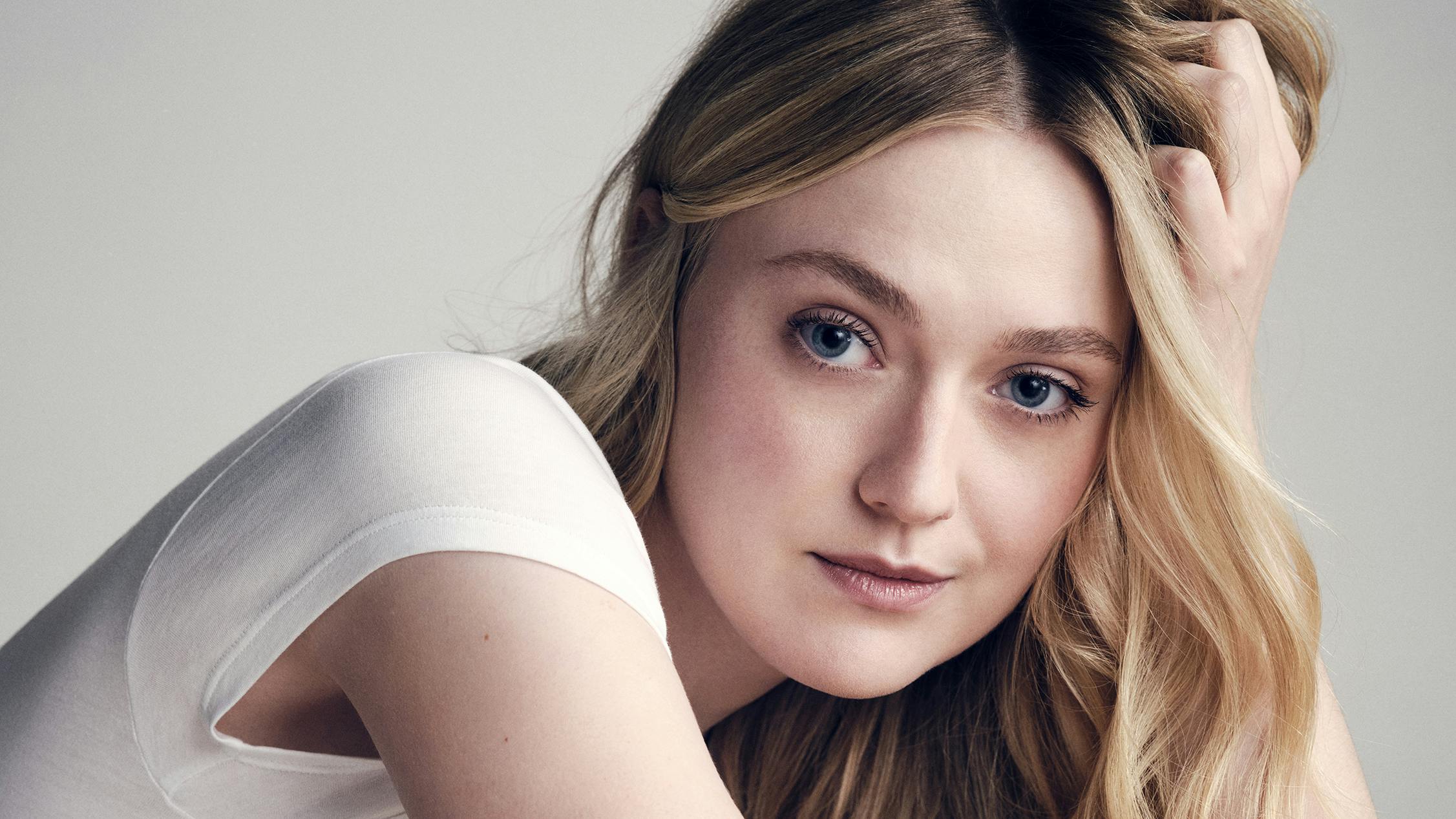 Dakota Fanning wears a white shirt and leans her blond head into her palm.