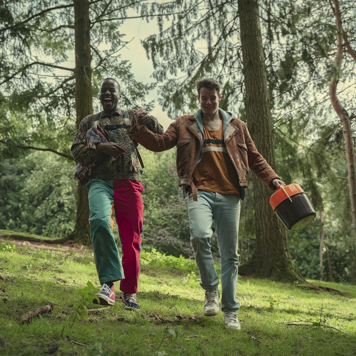 Eric Effiong (Ncuti Gatwa) and Adam (Connor Swindells) prance through a verdant forest scene.