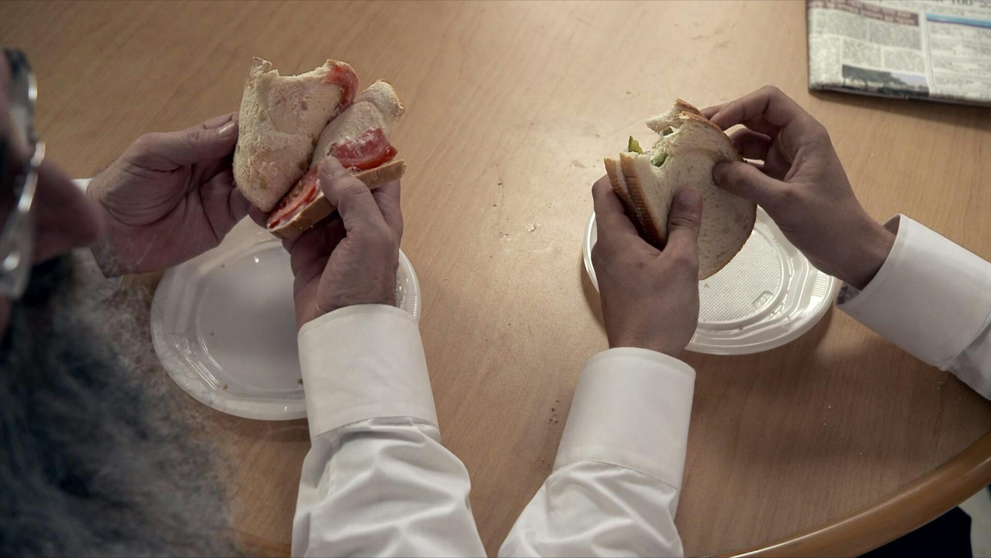 Shulem Shtisel (Doval’e Glickman) and Akiva Shtisel (Michael Aloni) reassemble their sandwiches. Akiva made two sandwiches, one with tomato and mayo and one with pickle and cheese. However, he mixed them up! Here they right this wrong, reuniting the tomato with the cheese, and the pickle with the mayo.