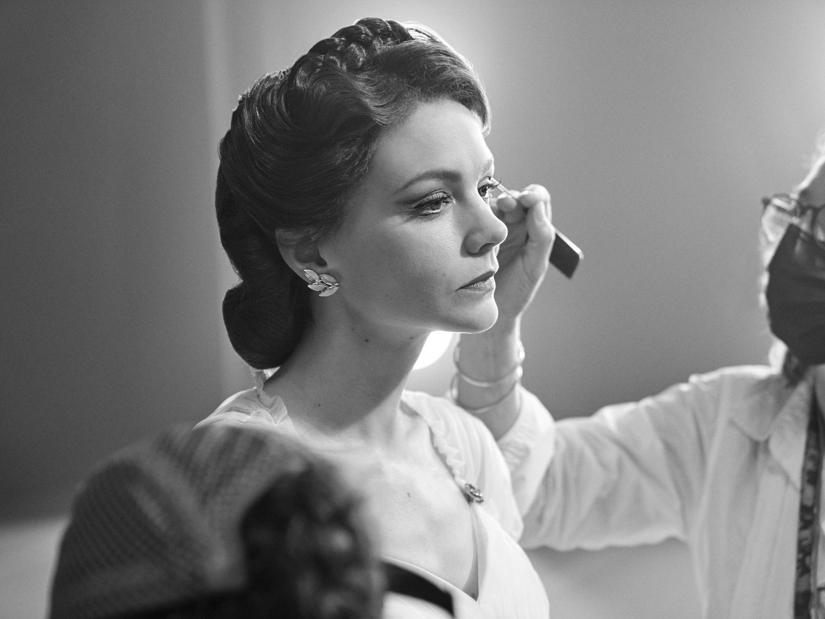 Carey Mulligan, behind the scenes, gets her makeup done by someone in a mask.