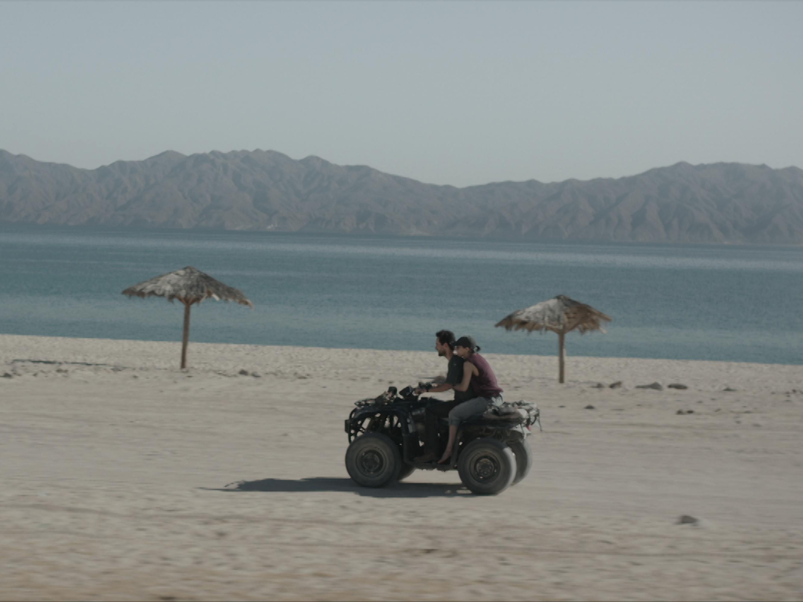 The couple from Camino a Marte race down an empty beach on an ATV four wheeler. 