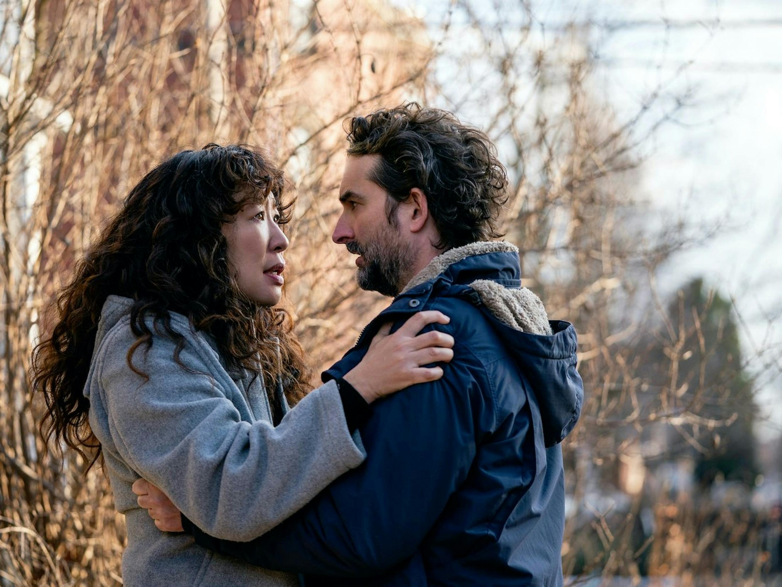 Dr. Ji-Yoon Kim (Sandra Oh) and Bill Dobson (Jay Duplass) embrace against a wintry scene. They both wear jackets and there is a bare tree behind them.