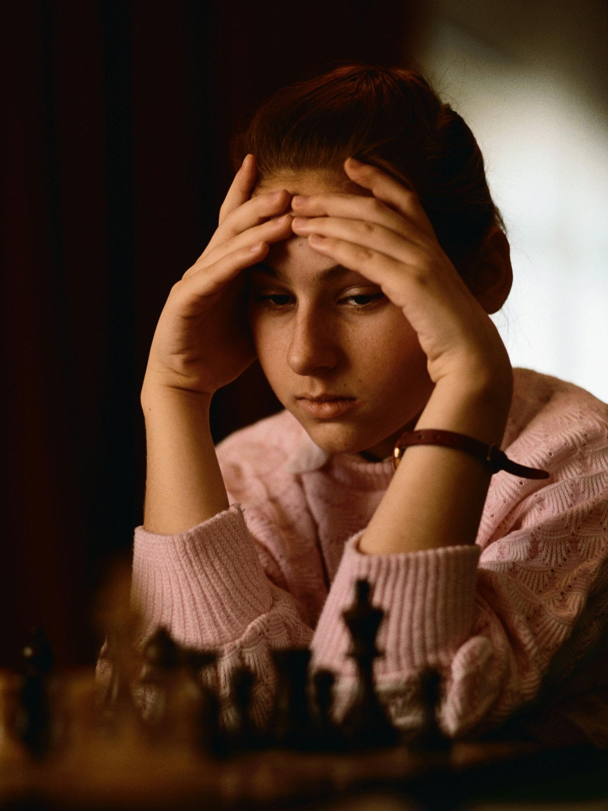 Polgár at age 12. Looking almost like a ballerina in a pink sweater, her hair pulled back, she stares pensively at a chess board.