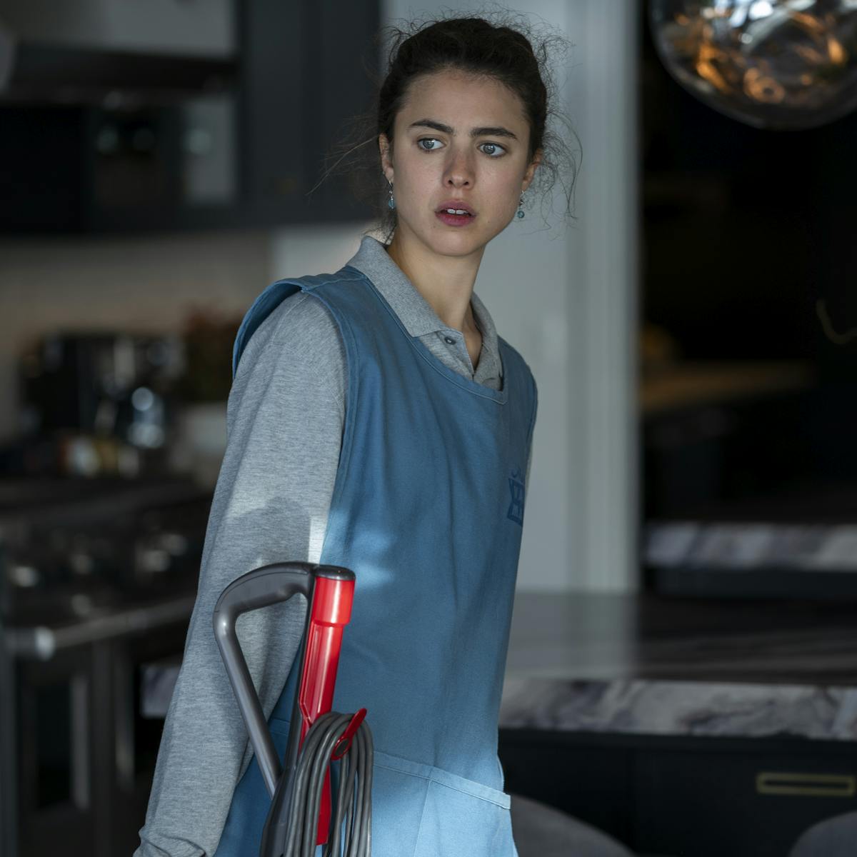 Alex Russell (Margaret Qualley) wears a maid uniform and carries a vacuum. 