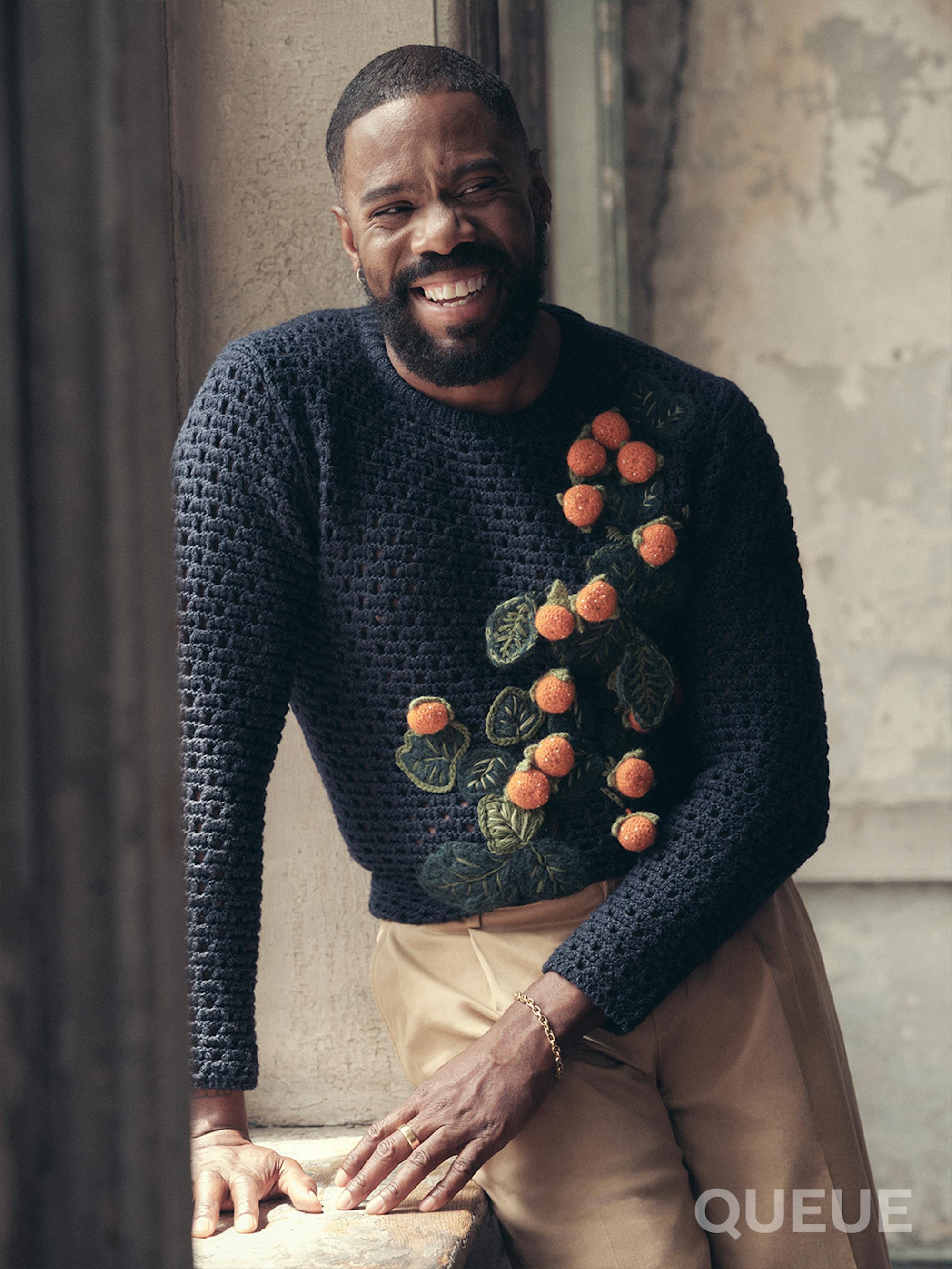 Colman Domingo wears khakis and a navy sweater with 3D oranges and leaves.