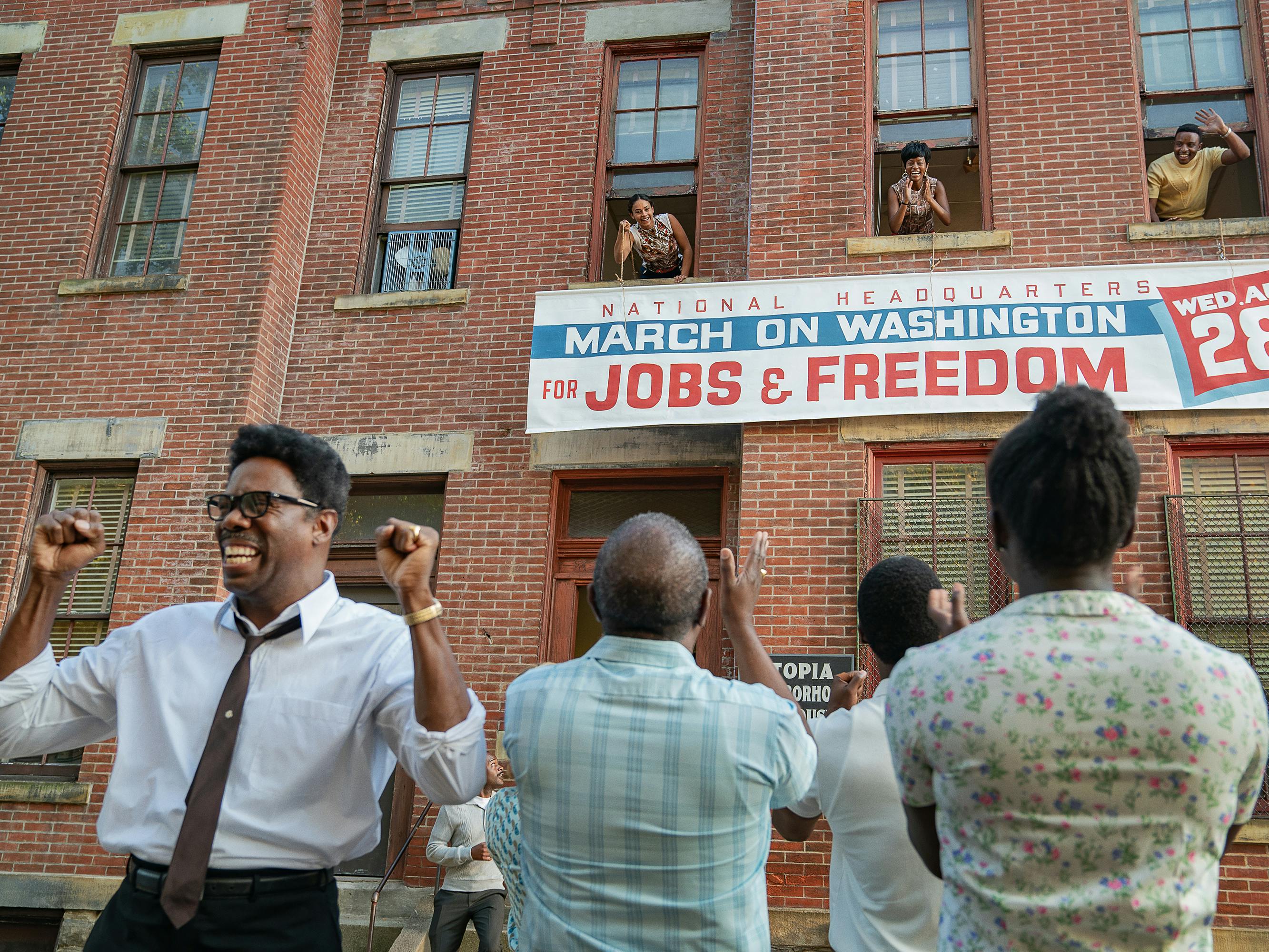 Bayard Rustin (Colman Domingo) celebrates the march outside a brick building. 