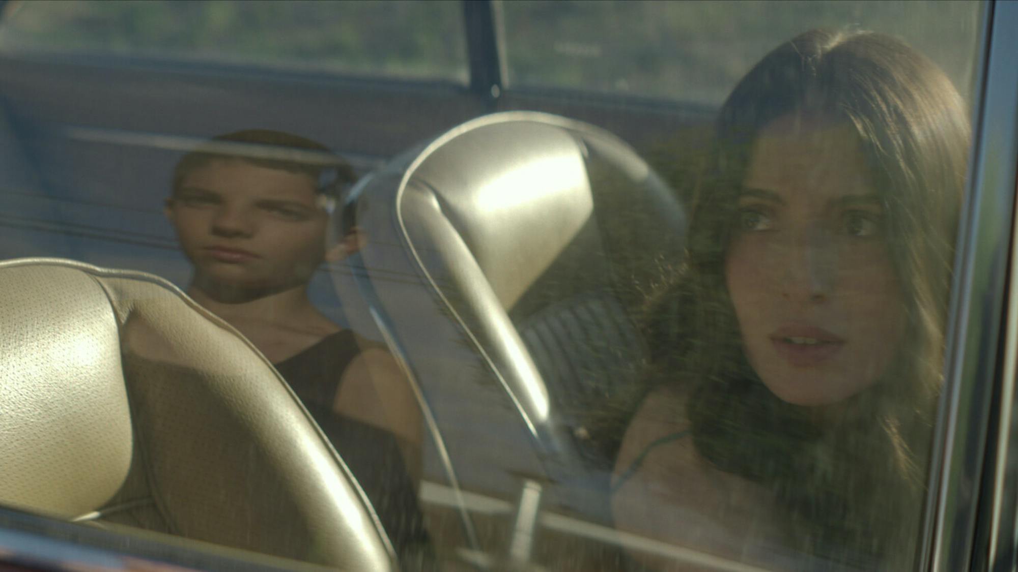 David (Emilio Vodanovich) and Amanda (María Valverde) look at each other through the car window. David appears as a reflection in the window, and Amanda looks nervous.