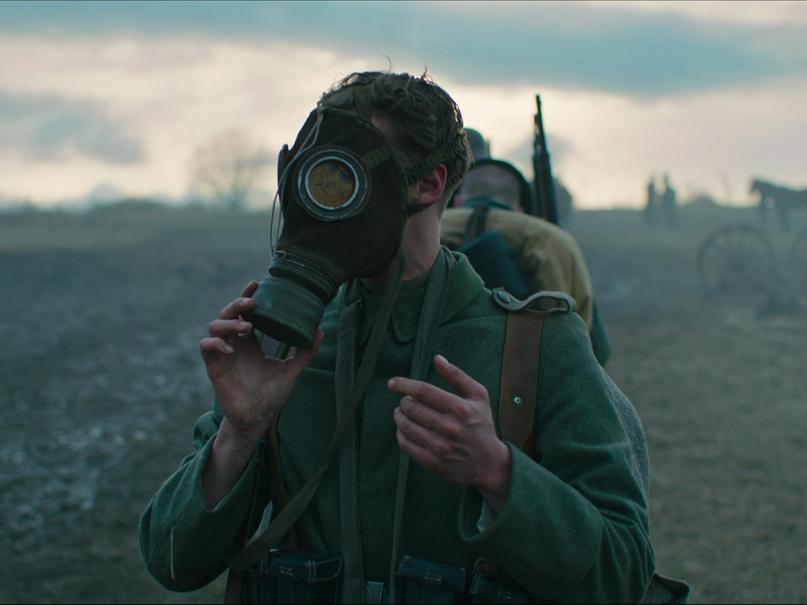 Paul Bäumer (Felix Kammerer) wears his bug-like gas mask as he walks in a line of other soldiers through a barren field.