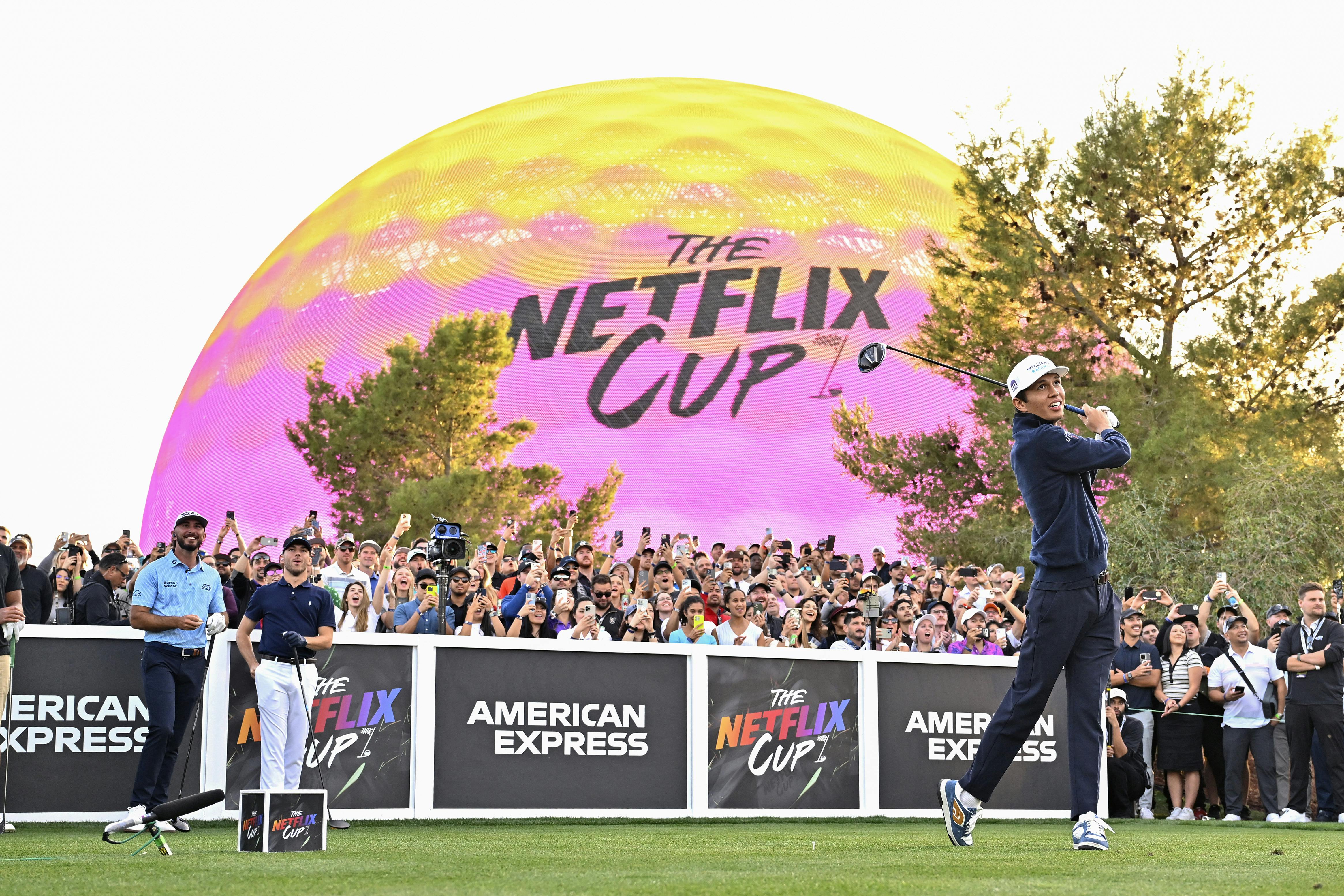 A massive yellow-and-pink golfball looms over a crowd of people as Alexander Albon swings.