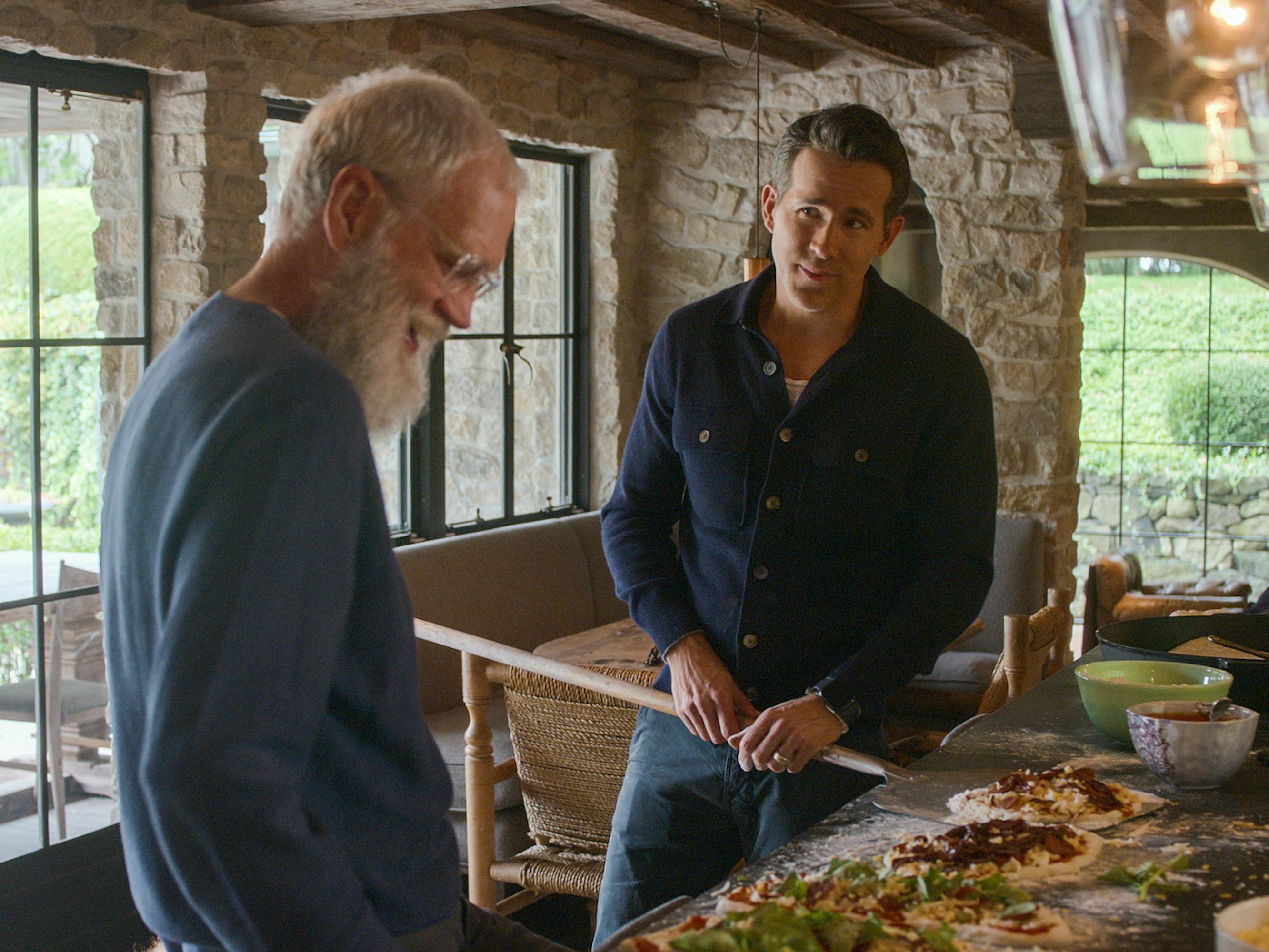 David Letterman and Ryan Reynolds stand in front of a delicious spread of pizzas.