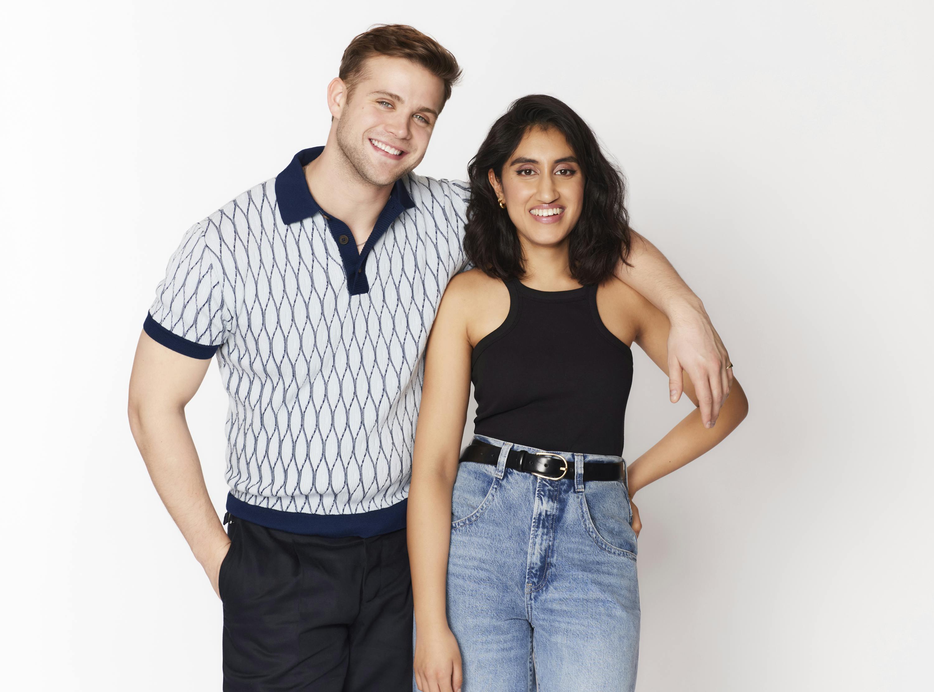 Leo Woodall and Ambika Mod pose together against a white background. He wears a patterned polo shirt and dark pants. She wears jeans and a black racerback tank.