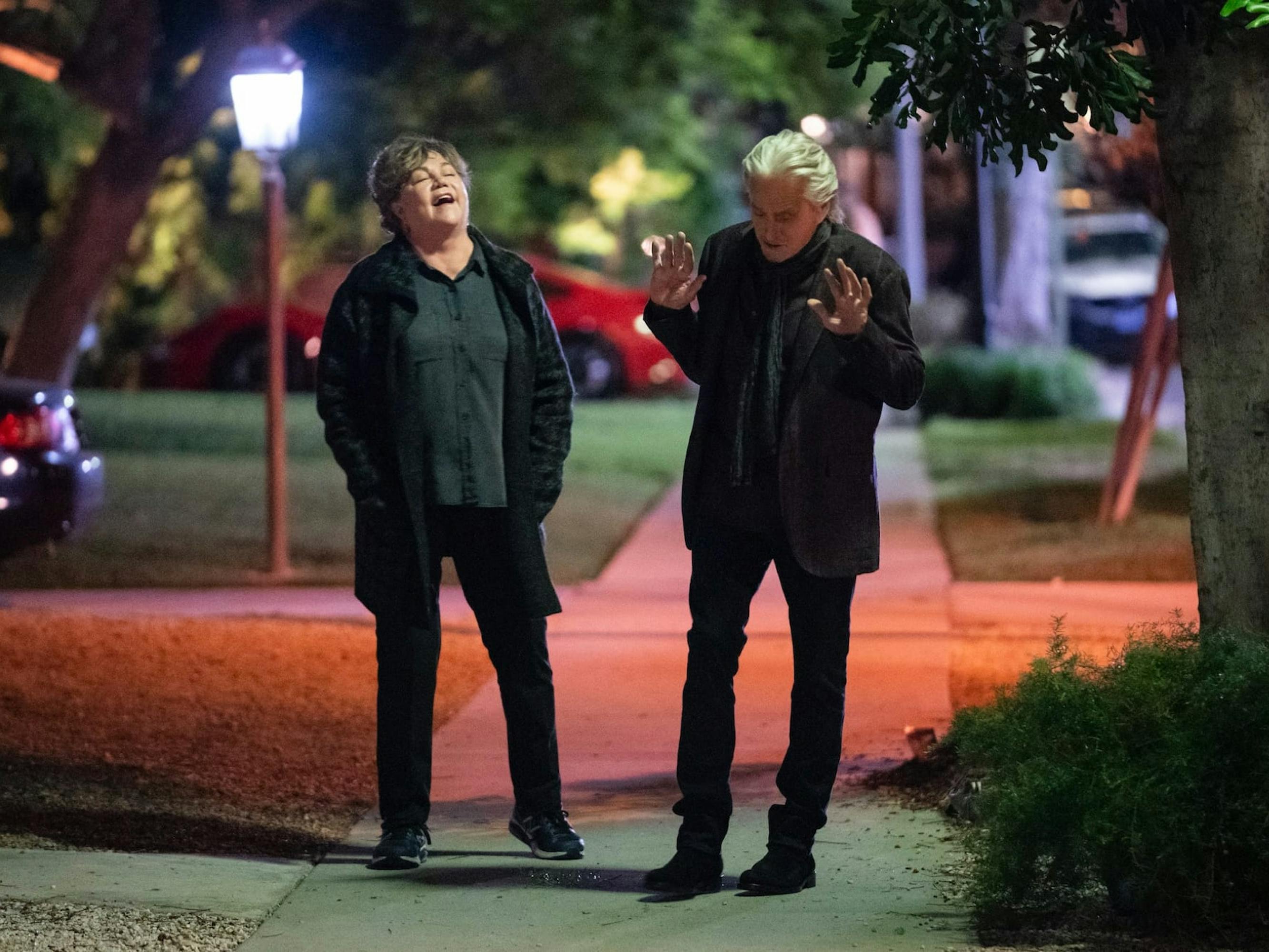 Roz (Kathleen Turner) and Sandy Kominsky (Michael Douglas) in The Kominsky Method walk down the sidewalk talking and laughing.
