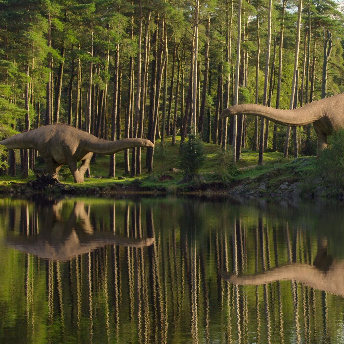 Two dinosaurs stand by a still body of water in a verdant green clearing.
