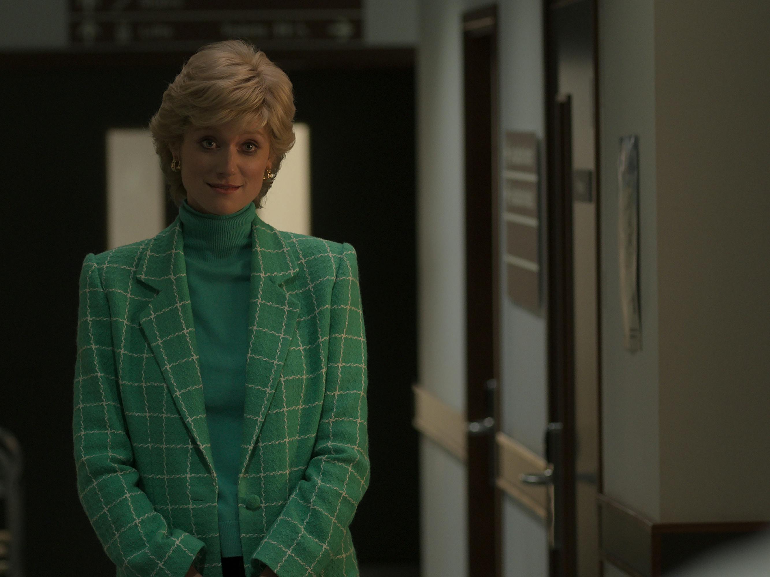 Princess Diana (Elizabeth Debicki) stands in a hospital wearing a green turtleneck and plaid jacket. 