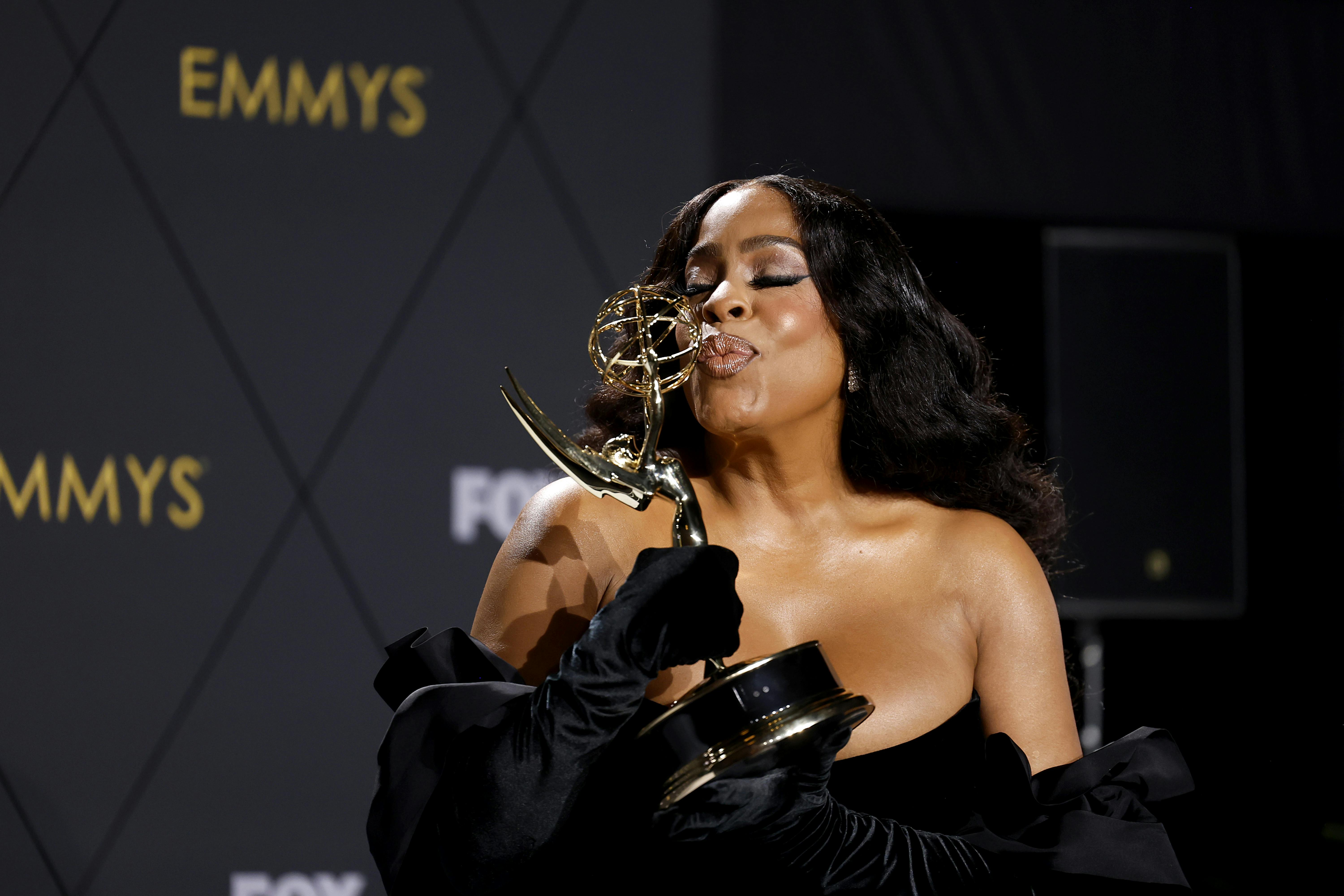 Niecy Nash-Betts wears a strapless black dress and kisses her Emmy award.