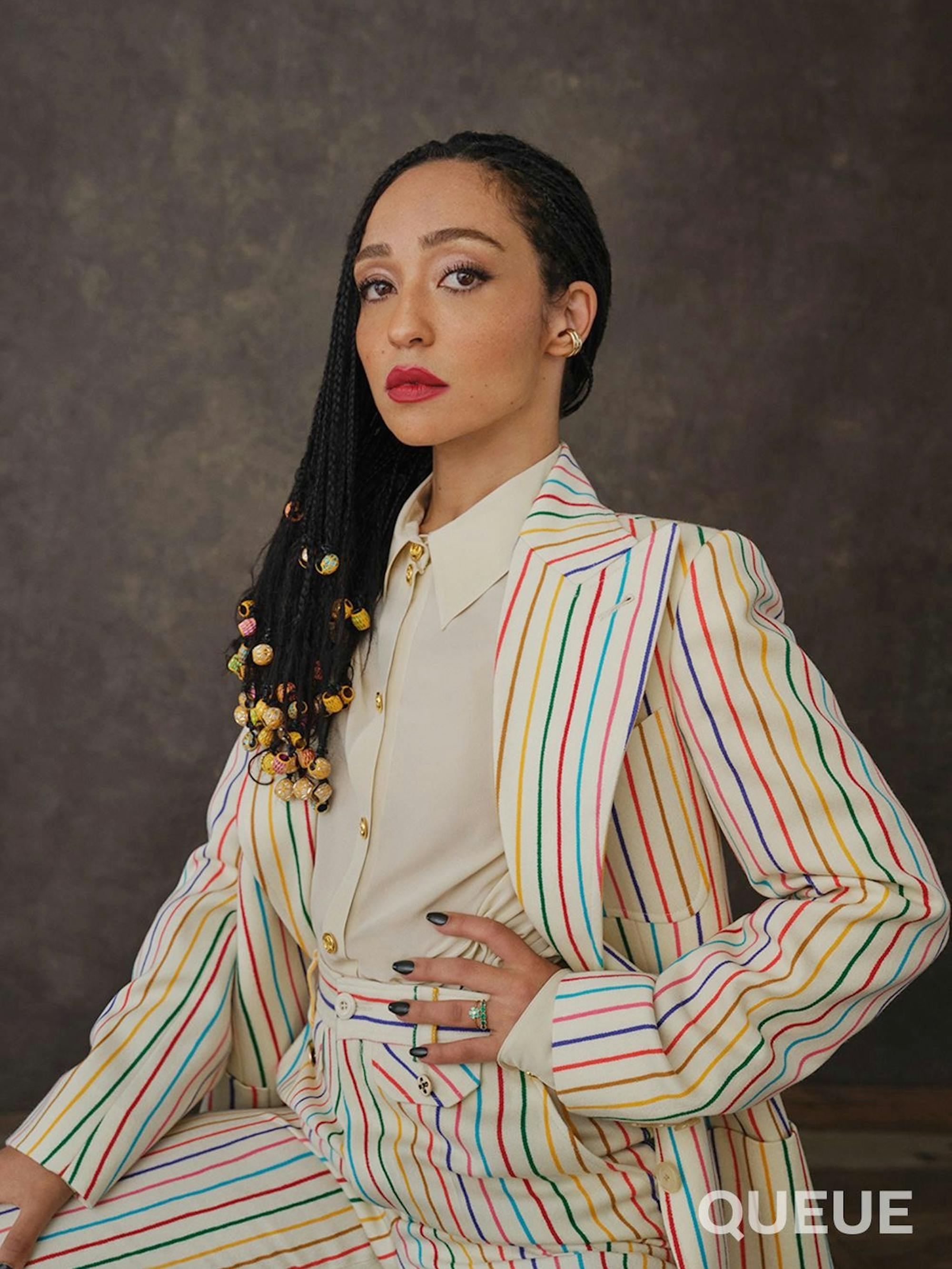 Ruth wears a rainbow striped suit and white blouse.