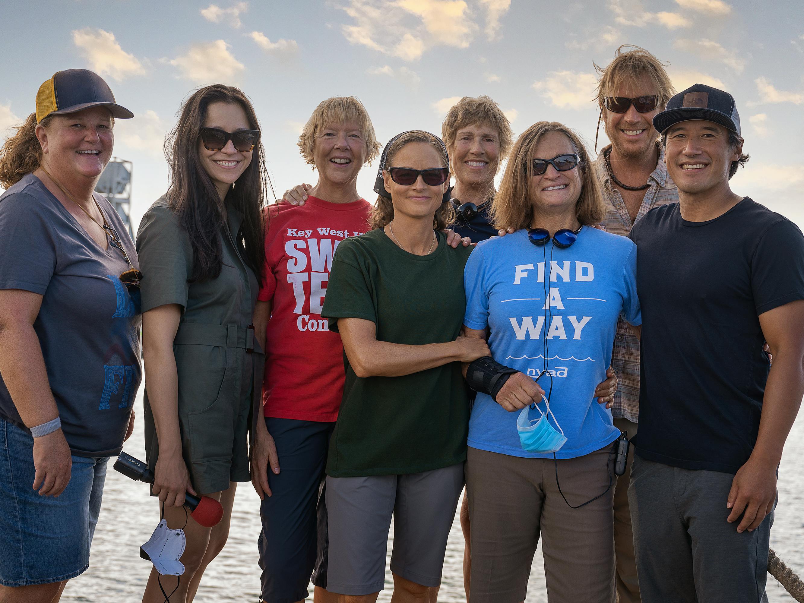 Karly Rothenberg, Elizabeth Chai Vasarhelyi, Annette Bening, Jodie Foster, Diana Nyad, Bonnie Stoll, Rhys Ifans, and Jimmy Chin stand together on a dock smiling for the camera.