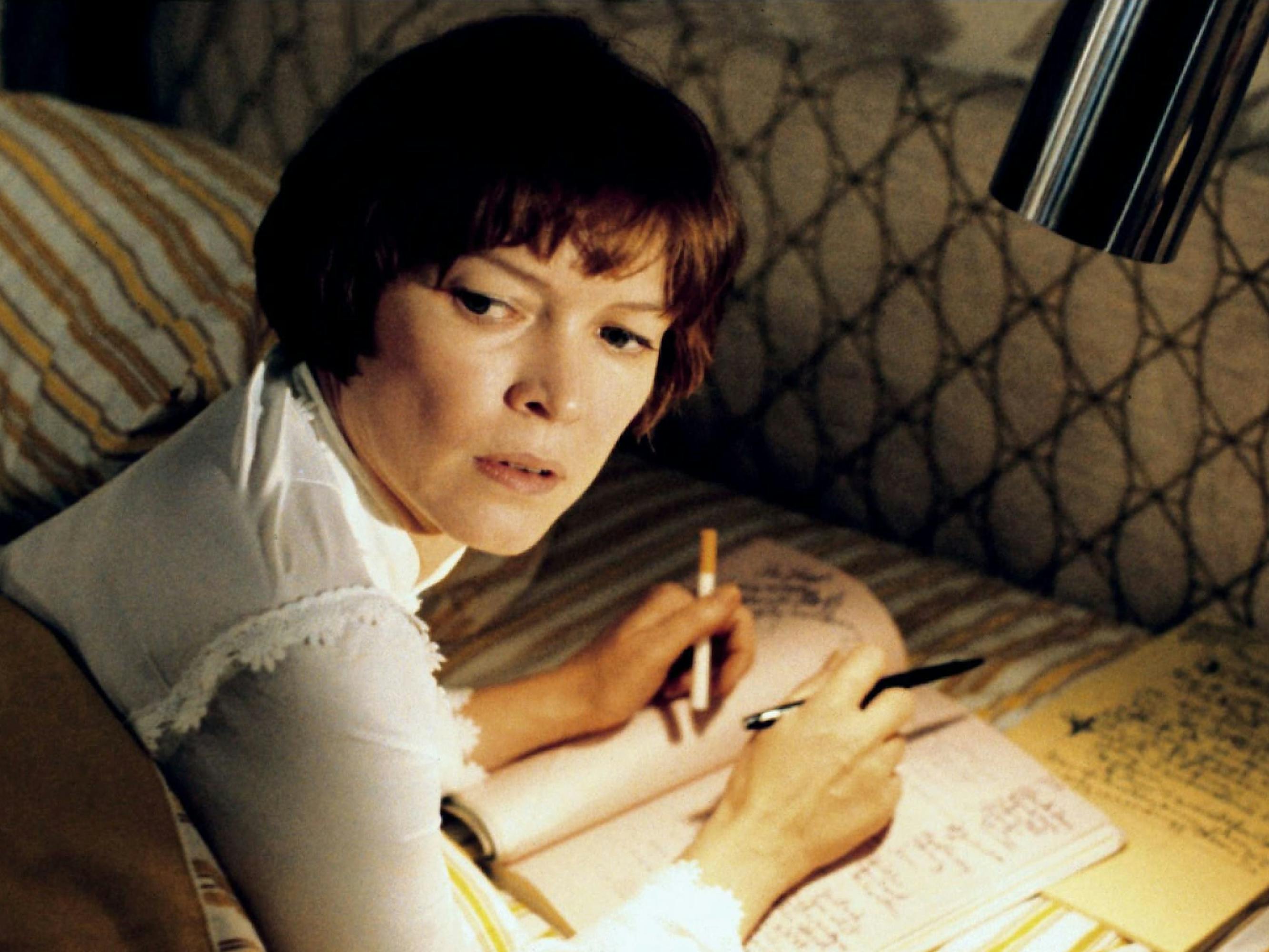 Ellen Burstyn as Chris MacNeil in a still from The Exorcist. She’s lying in bed, writing in a notebook. She looks up, alarmed.