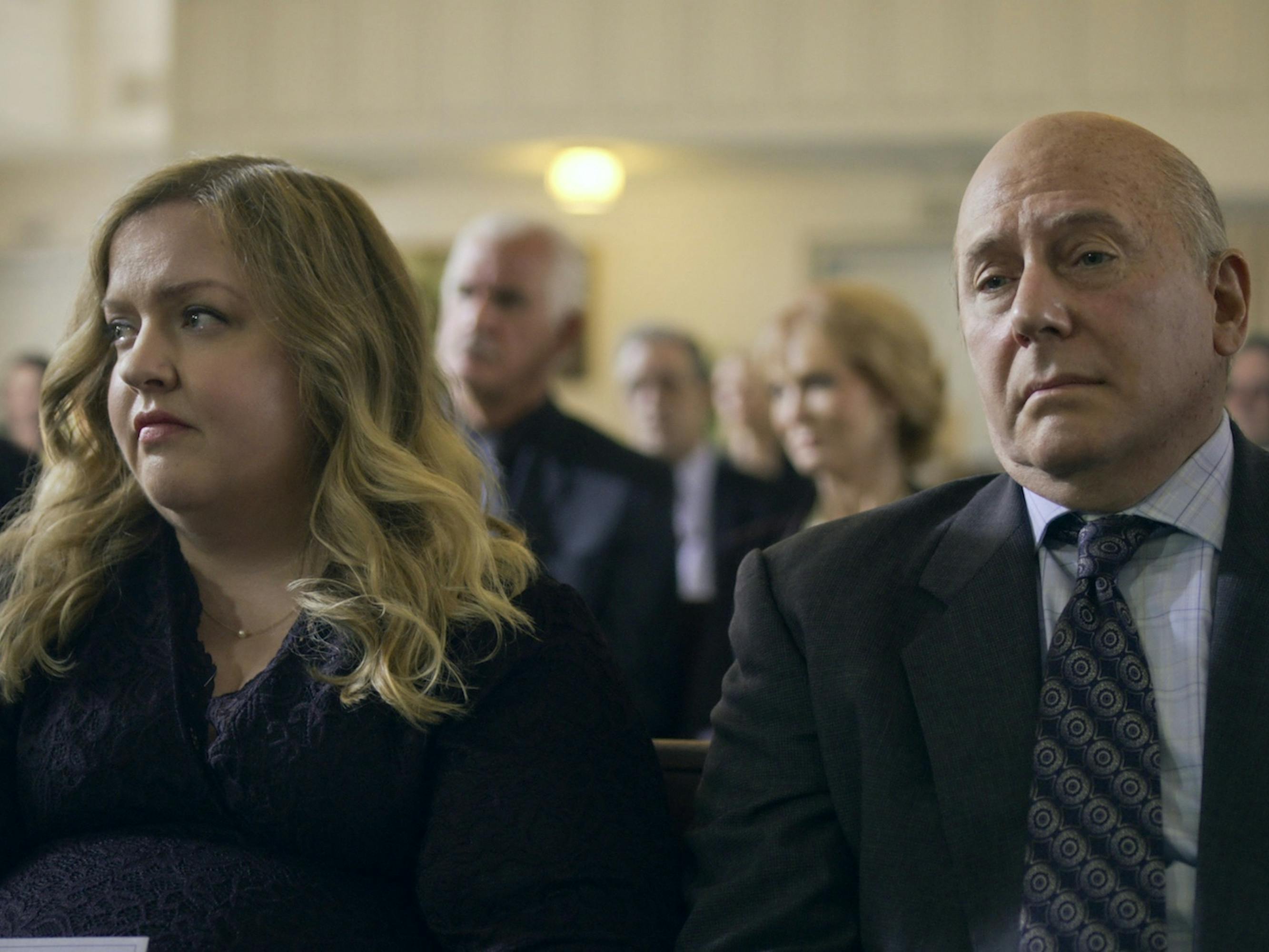 Mindy Kominsky (Sarah Baker) and Martin (Paul Reiser) wear funeral garb and sit in a church pew.