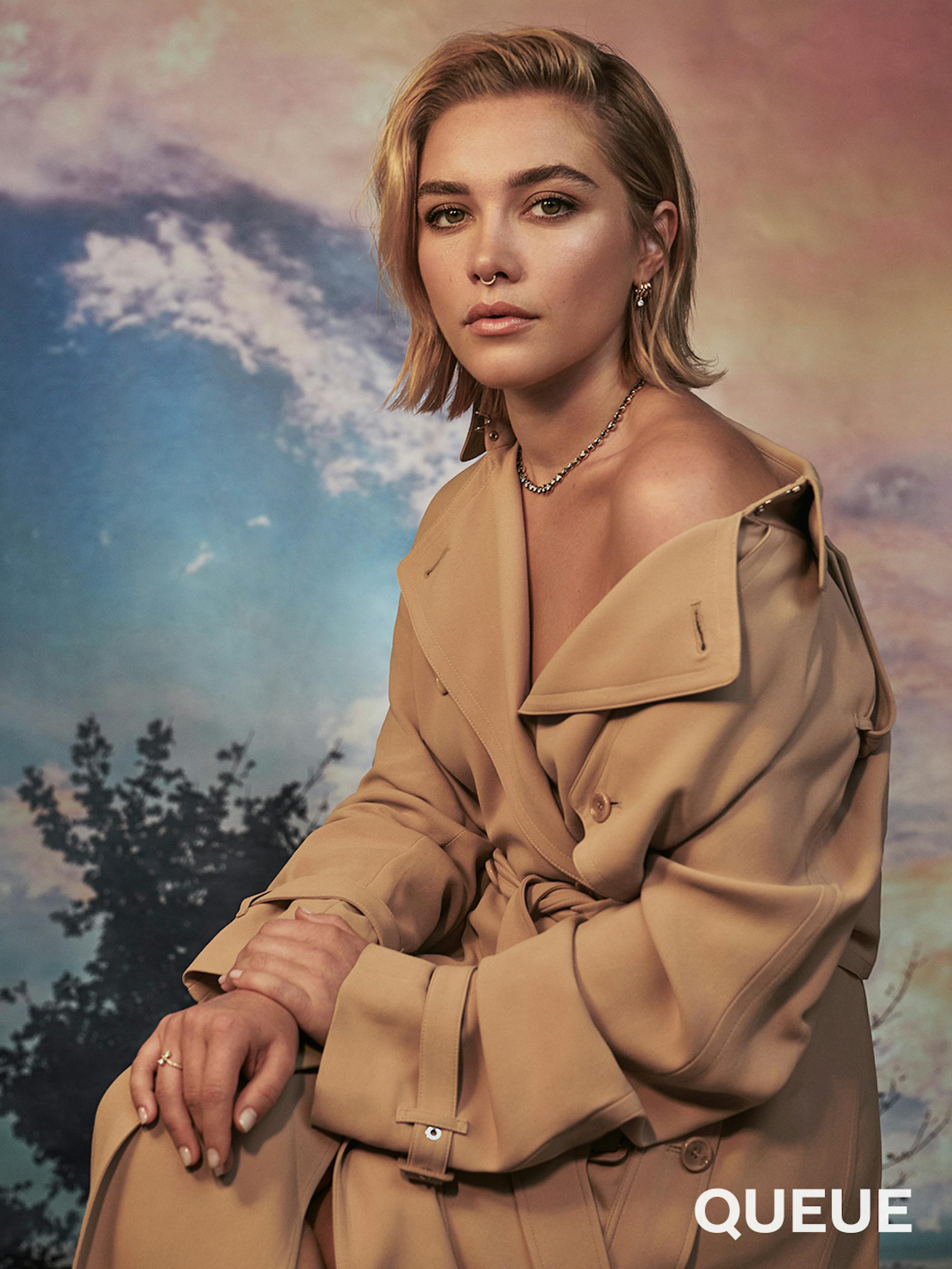 Florence Pugh wears a khaki dress and stands in front of a colorful background.