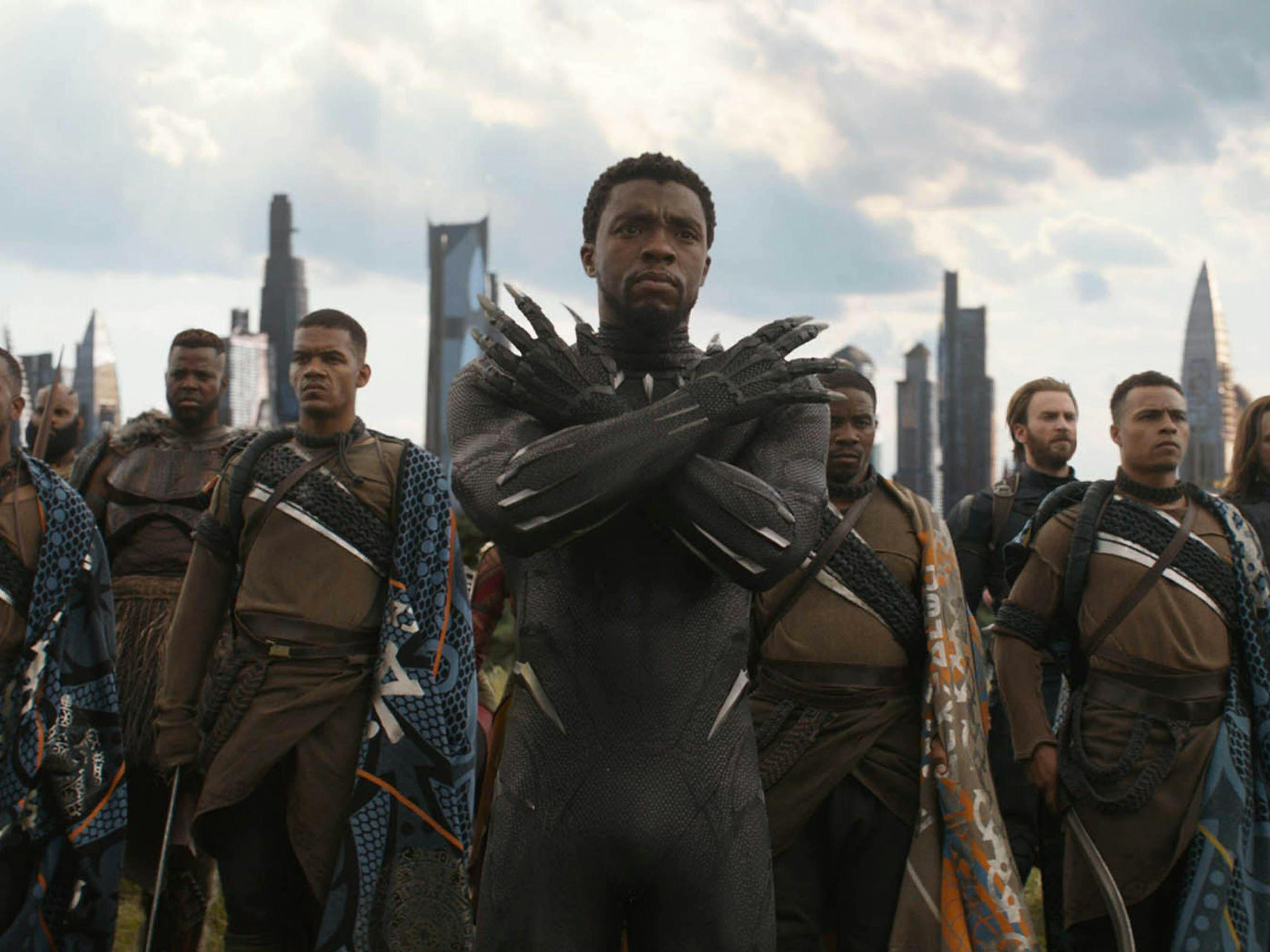 Chadwick Boseman as T’Challa, wearing his sleek suit. He is flanked by other warriors, and Wakanda’s skyline is in the background. He looks ready for battle.