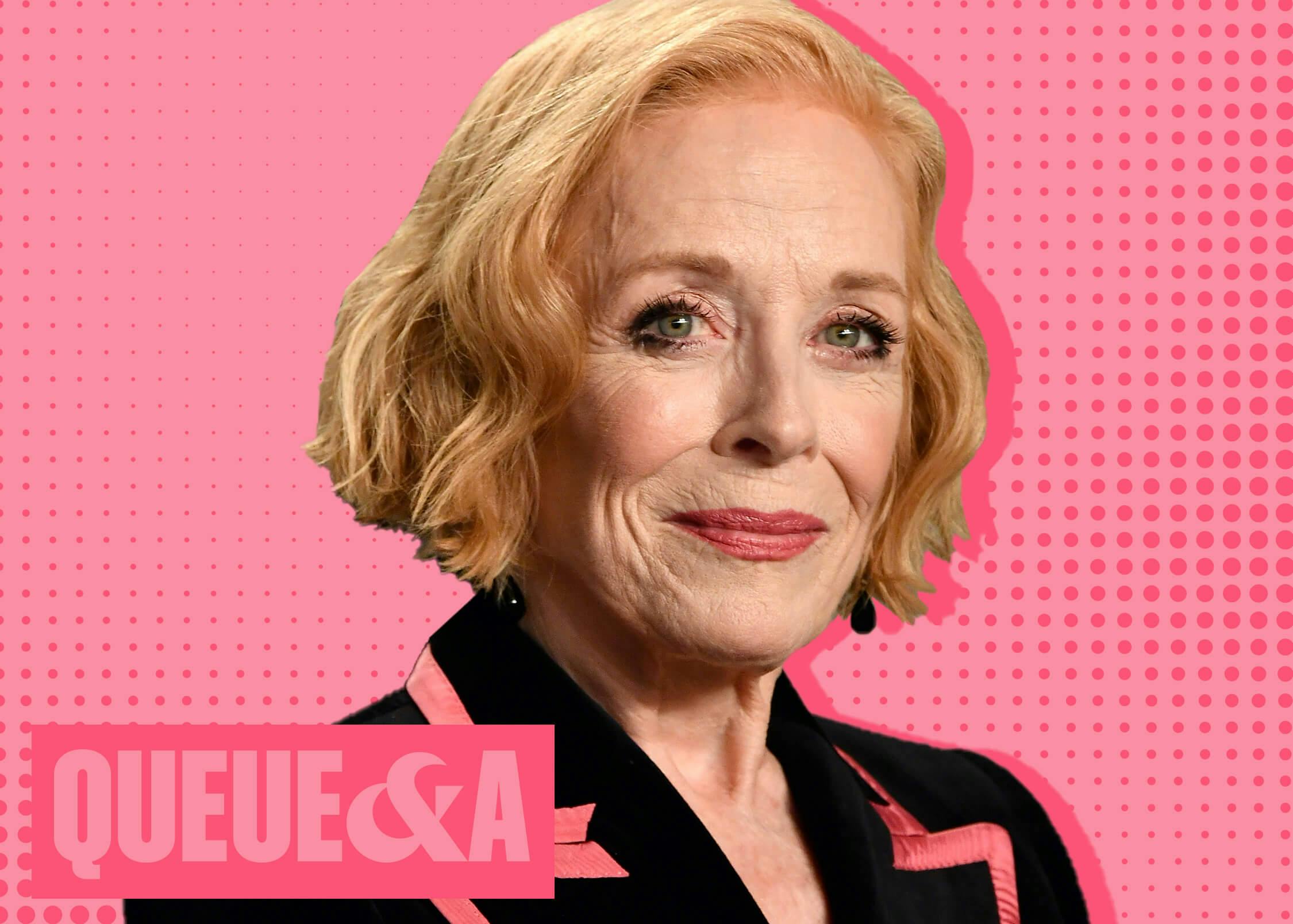 Holland Taylor wears a black blazer trimmed with pink as she smiles slightly. The background is light pink dotted with dark pink and the bottom left corner reads Queue & A.