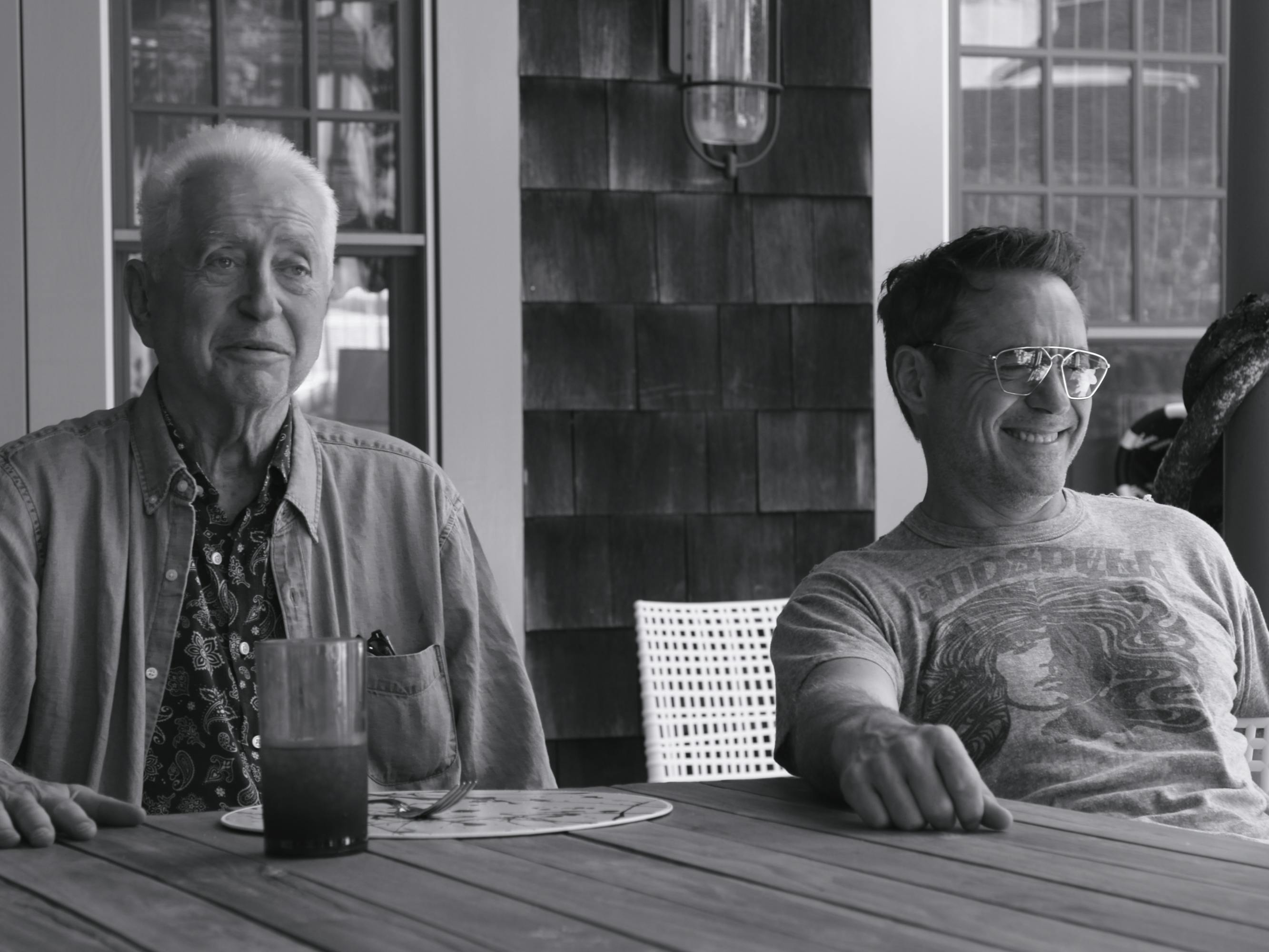 Robert Downey Sr. and Robert Downey Jr. sit together at a wooden table smiling and laughing.