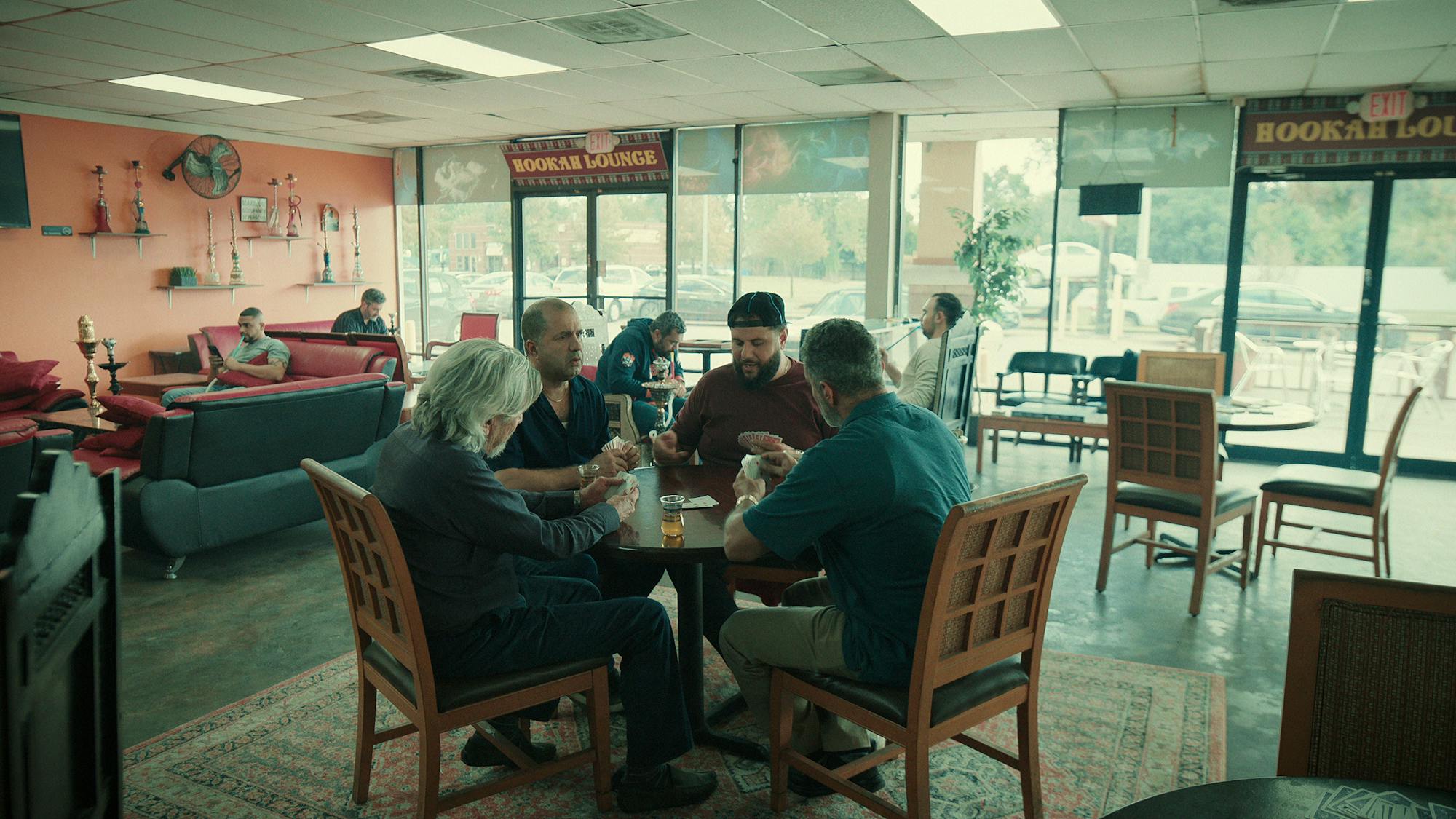Aba (Alan Rosenberg), Nazeer (Kamal Zayed), Mo (Mo Amer), Abood (Bassem Youssef) sit around a table playing cards in a hookah lounge. 