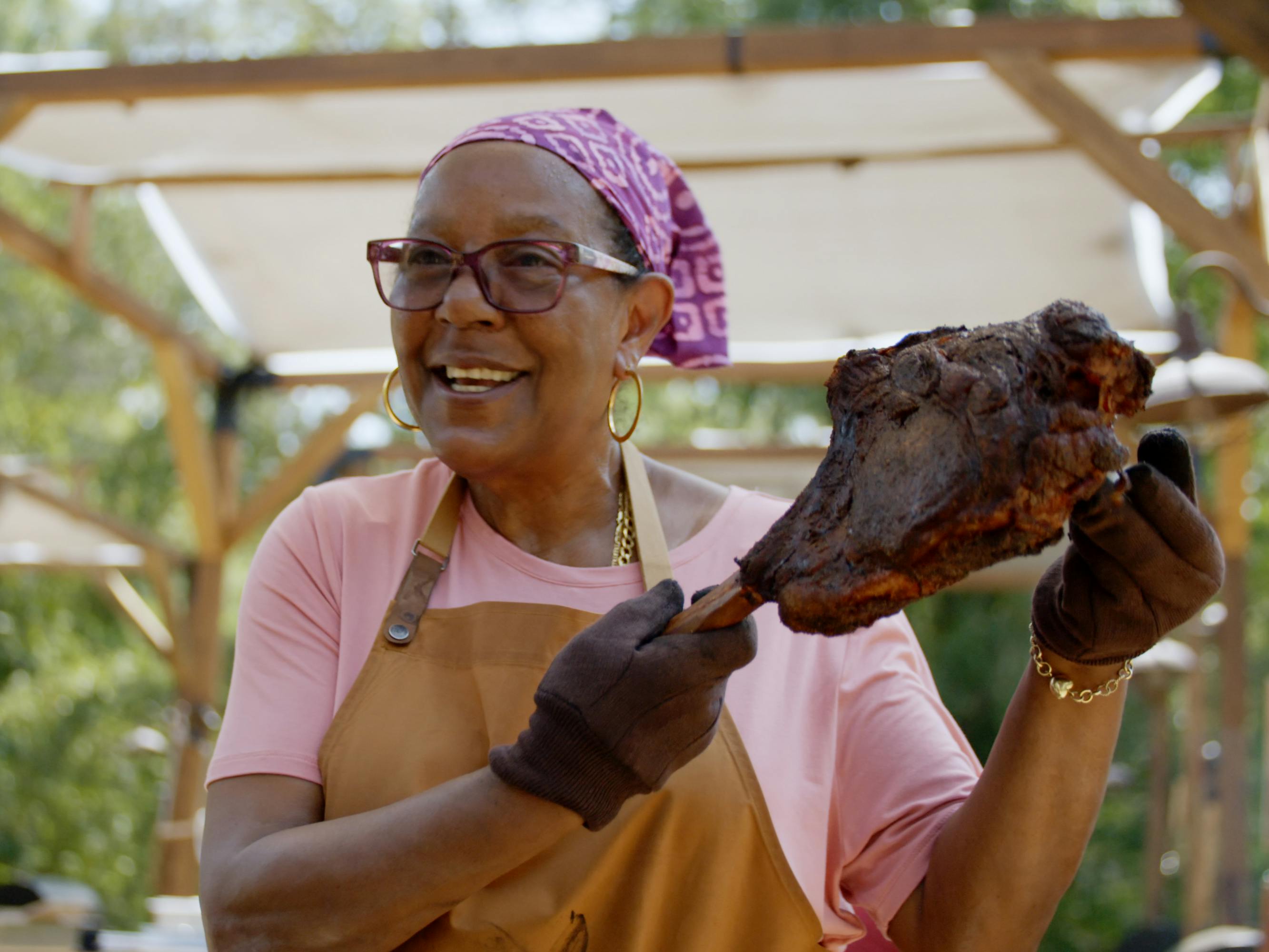 Sylvie Currie brandishes a leg of meat, wearing a purple hanker-chief and brown apron.