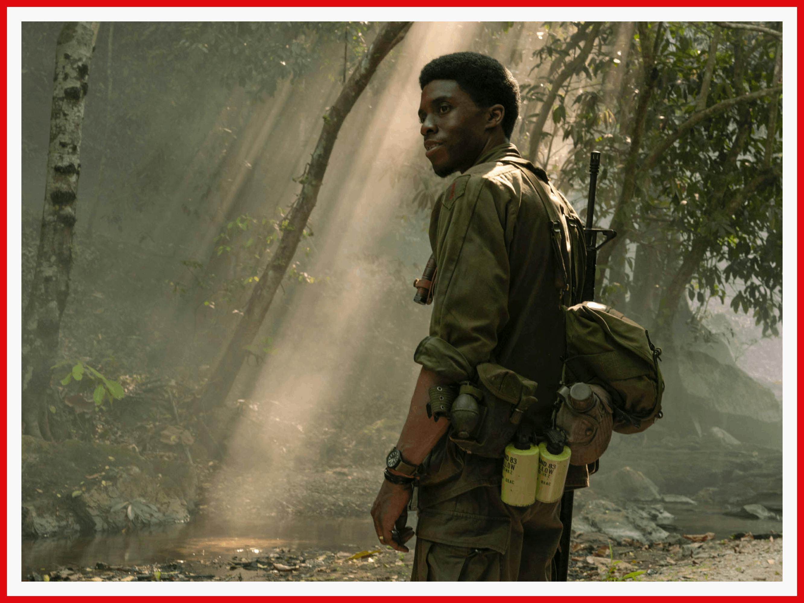 Chadwick Boseman is dressed in military fatigues and standing in dappled jungle light during one of the film’s flashback sequences