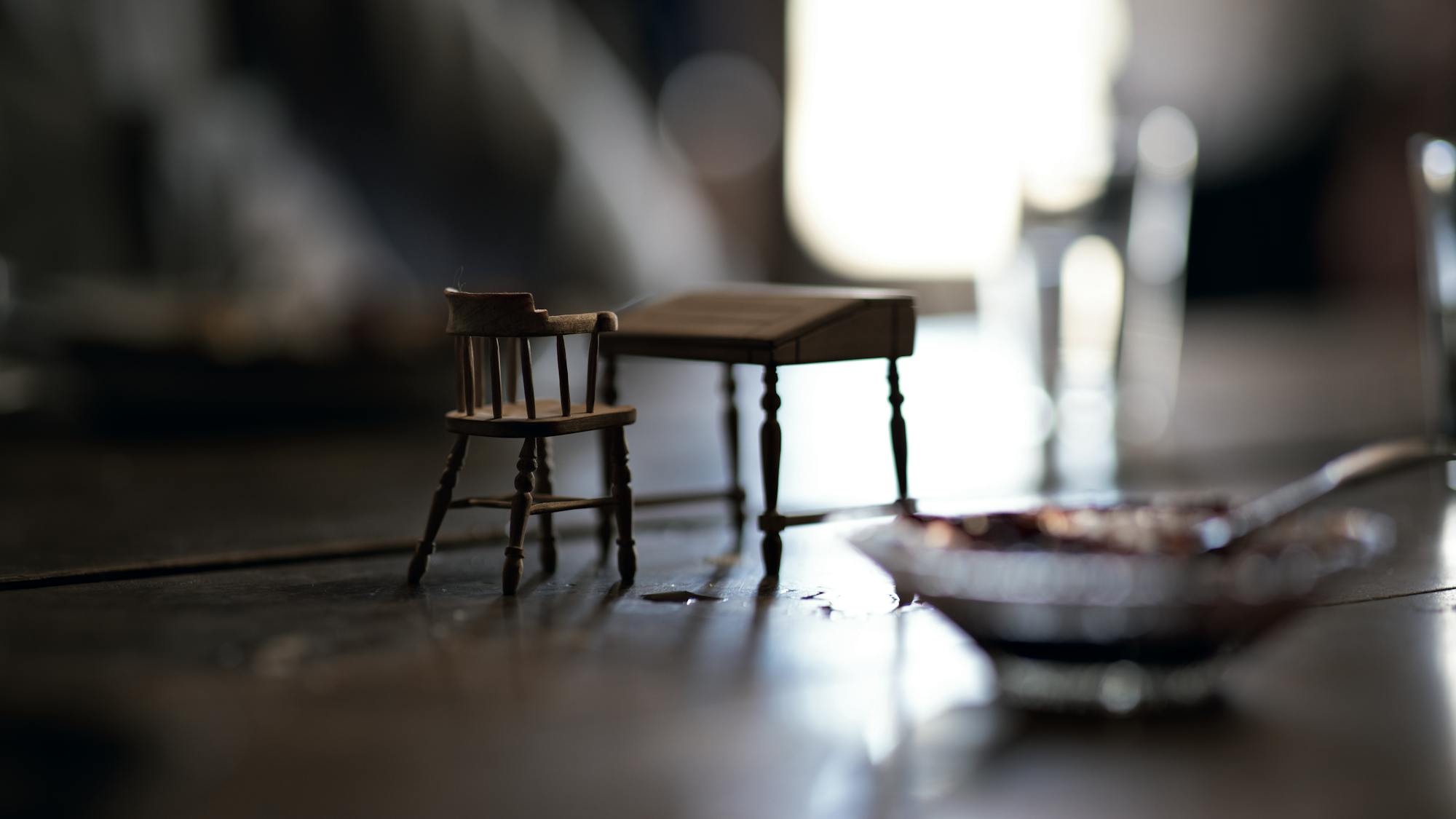 A miniature desk and chair sit on a wood table.