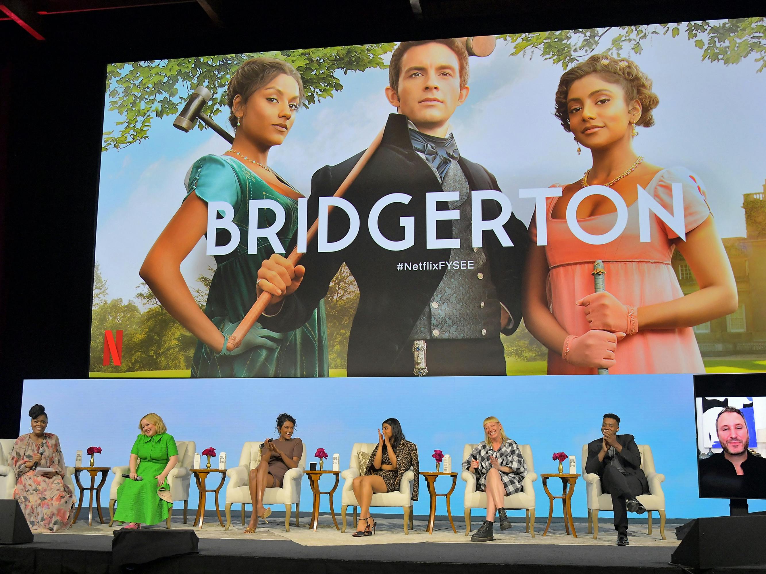 The Bridgerton title credit projected on the big screen over the panel's participants. From left to right: Yvette Nicole Brown, Nicola Coughlan, Simone Ashley, Charithra Chandran, Sophie Canale, Kris Bowers, and Chris Van Dusen (virtually).