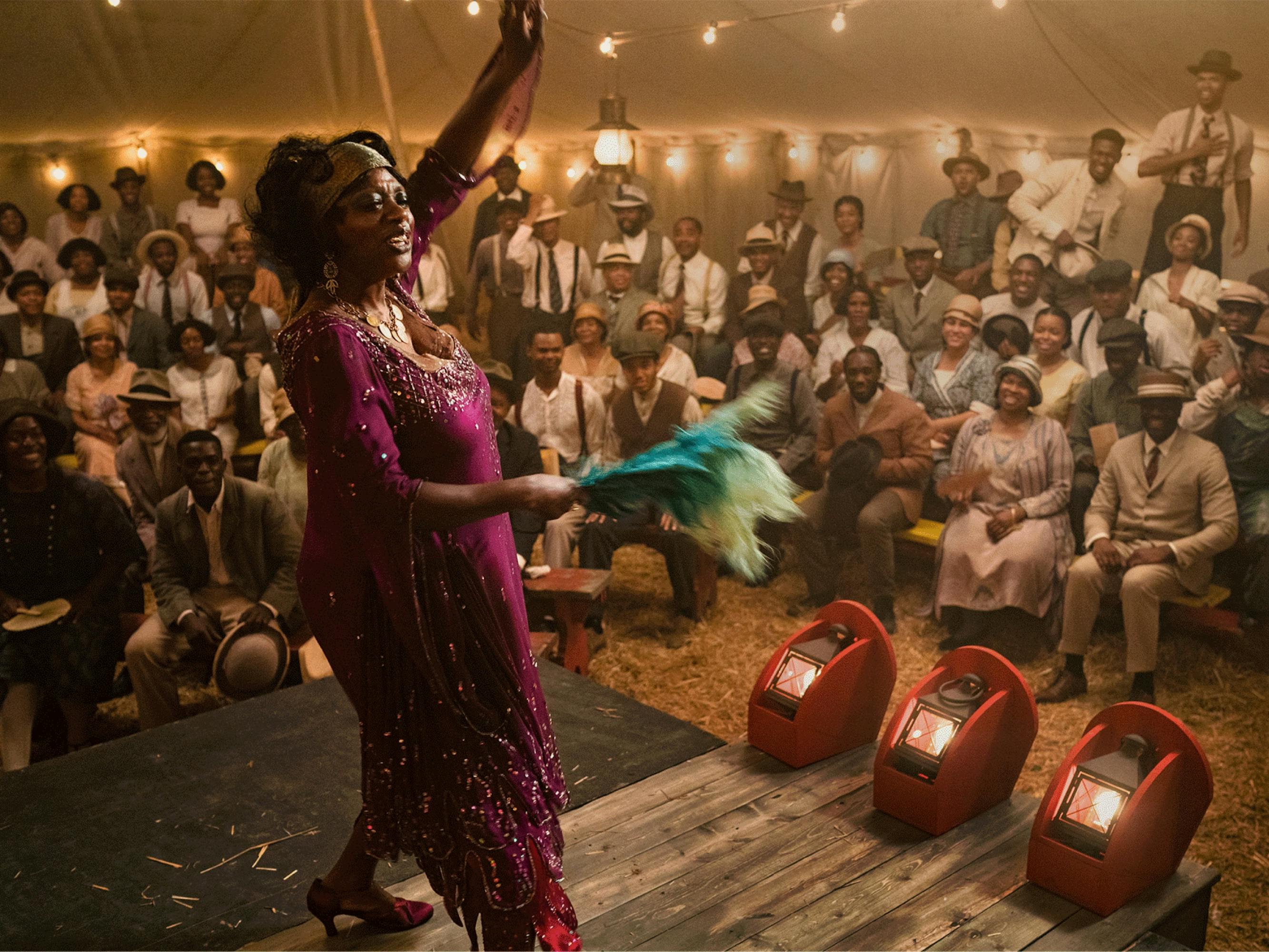 Ma Rainey (Davis) wears a deep magenta dress with glittering embellishment as she waves to an assembled crowd at a tent show in this still from Ma Rainey’s Black Bottom.