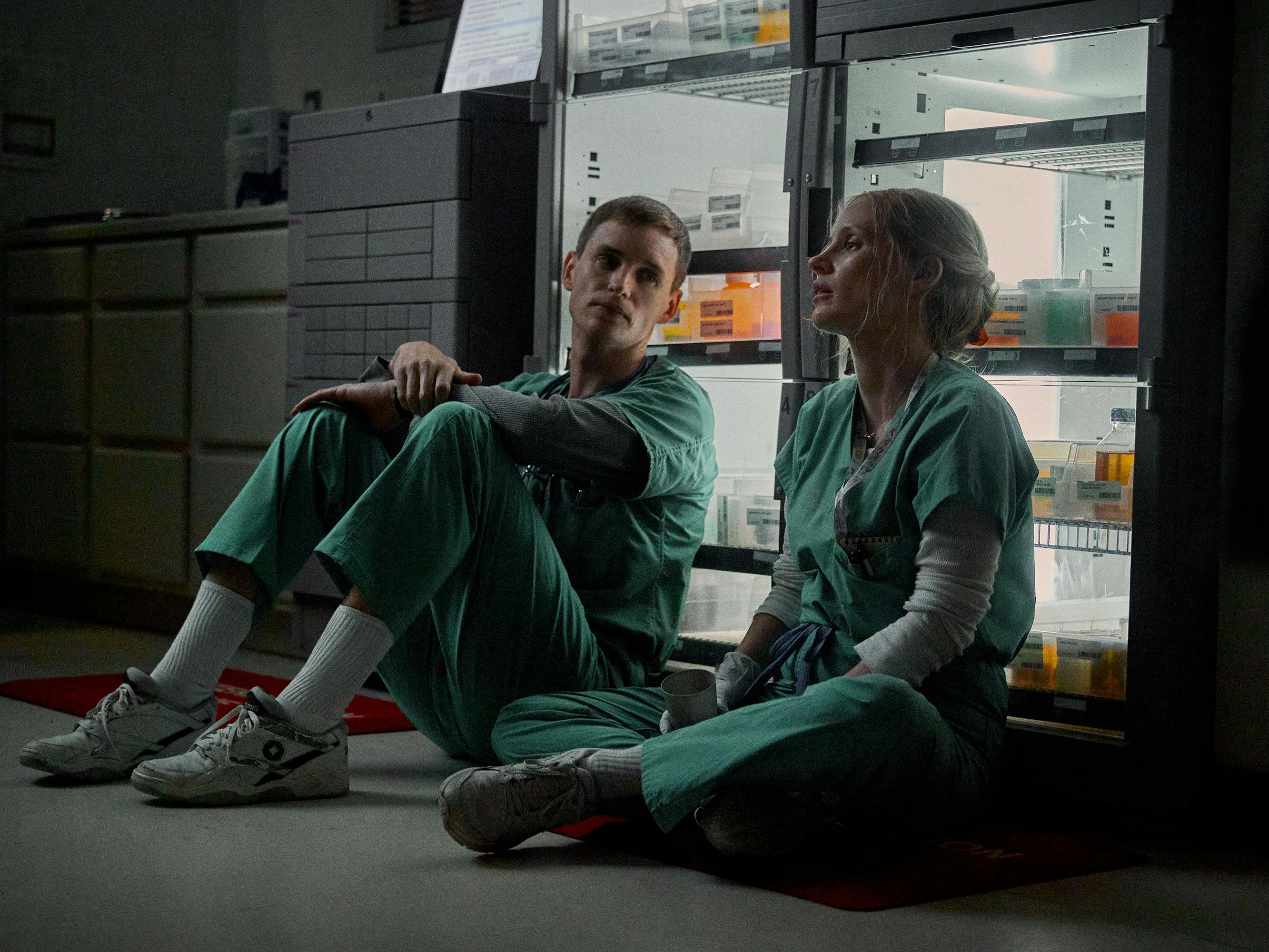 Charles Cullen (Eddie Redmayne) and Amy Loughren (Jessica Chastain) wear teal scrubs and sit against a medicine cabinet in a darkened hospital.