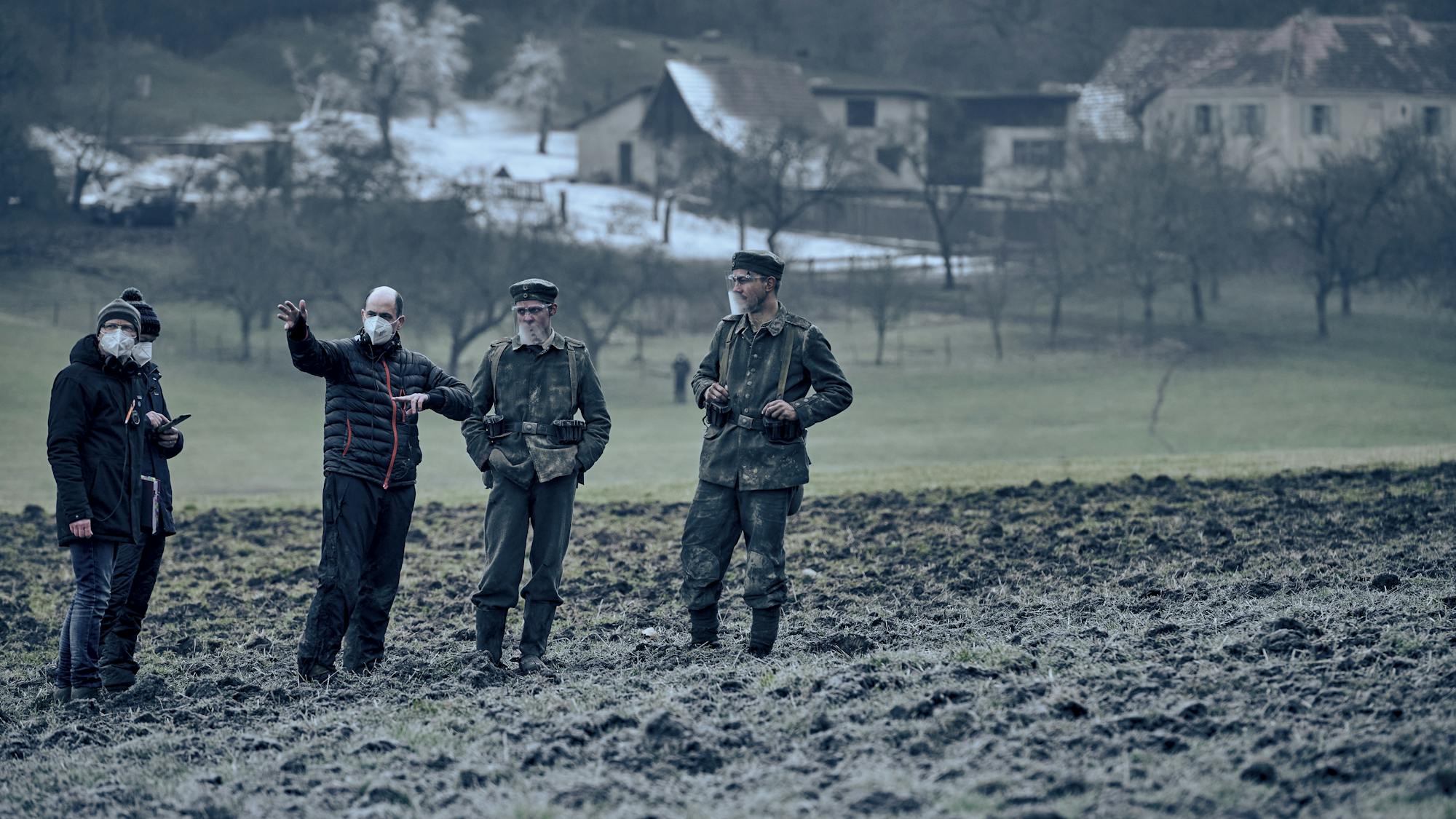 Director Edward Berger with actors Felix Kammerer and Albrecht Schuch stand together in a muddy field.